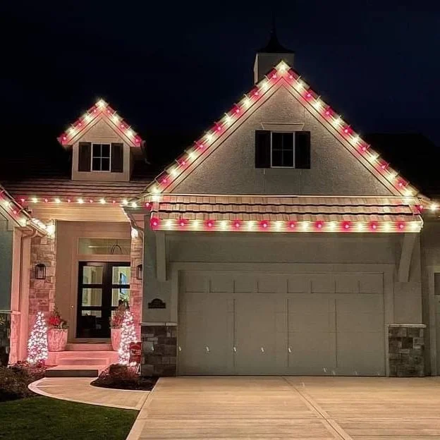 A house decorated with pink and white Christmas lights along the roofline at night.