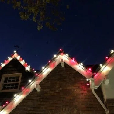 View of house rooftops decorated with Christmas lights at night, with a dark sky and visible stars above.