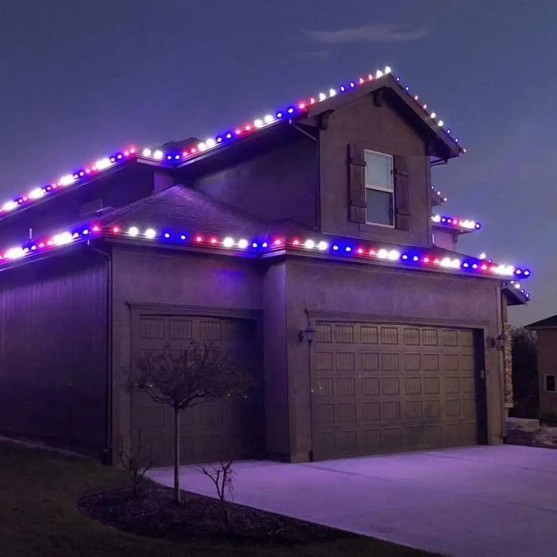 A two-story house at dusk decorated with colorful string lights outlining the roofline, creating a festive appearance.