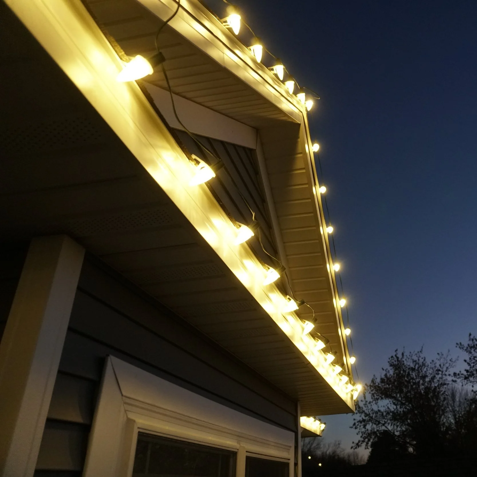 Exterior house with string lights hanging from the roof edge during dusk.