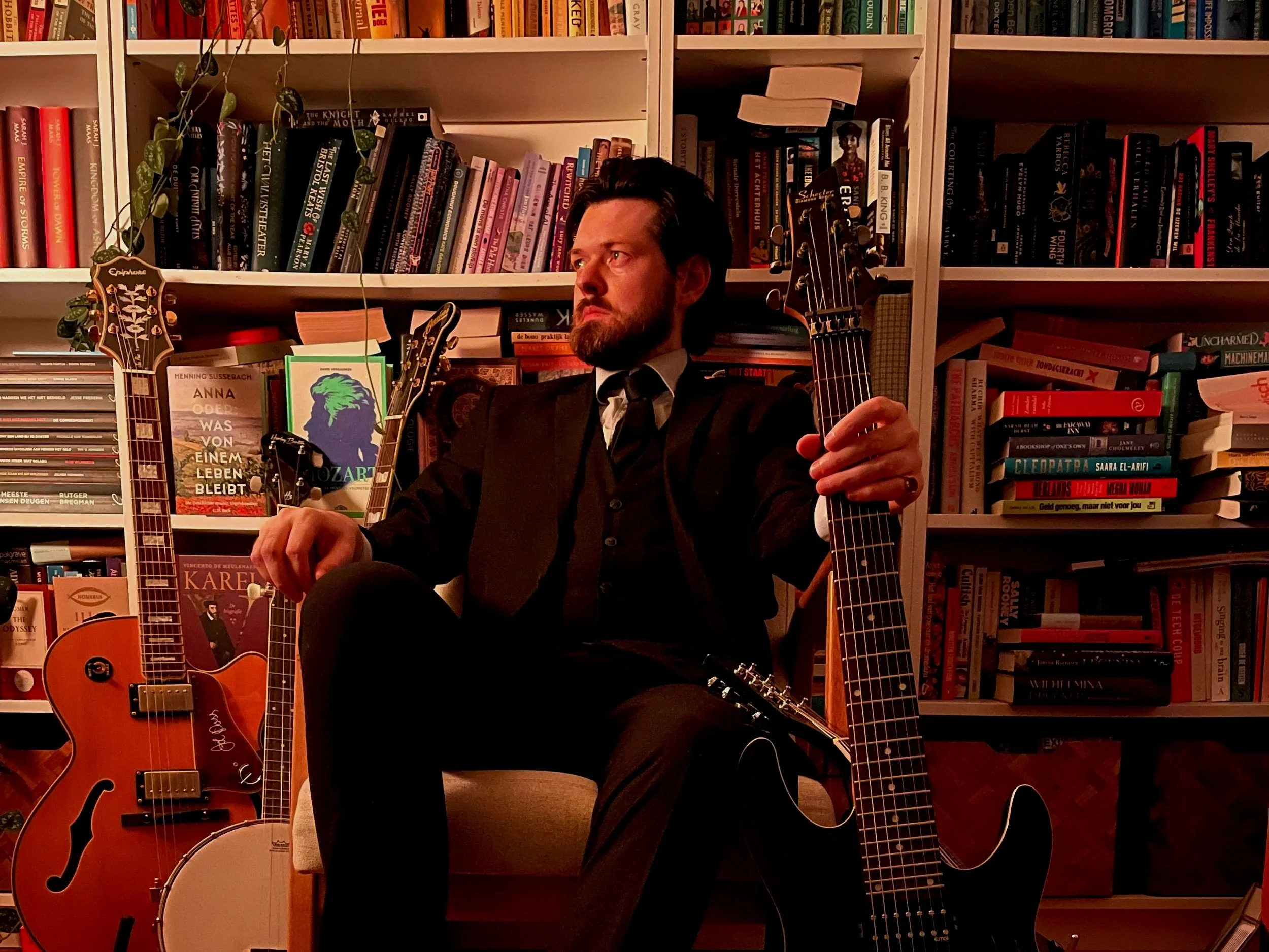Foto of Willem Sloet in a black suit and his instruments around him, a banjo, a mandolin, a jazz guitar, a semi acoustic guitar and a 7 string metal guitar