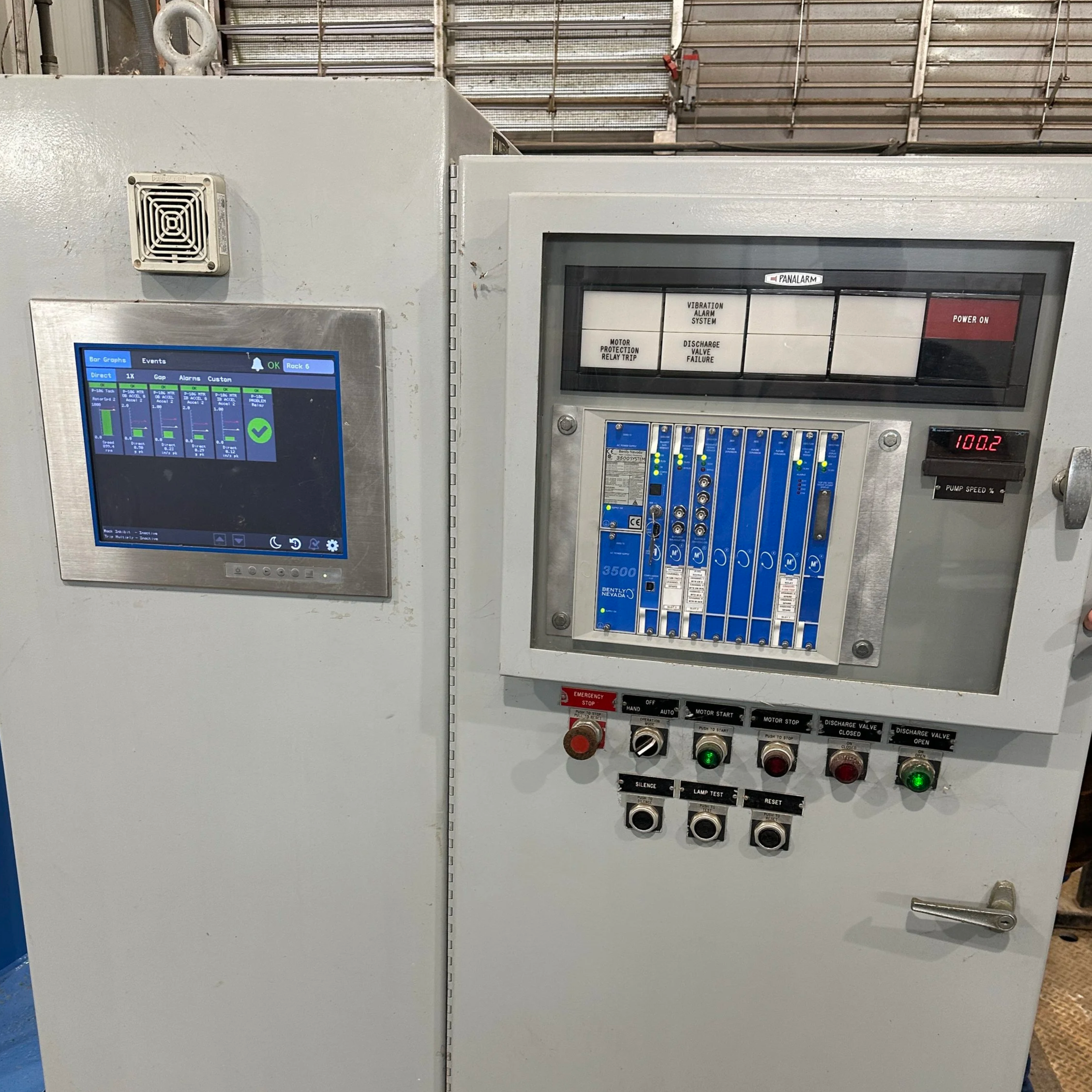 Electrical control panel with a digital screen, switches, buttons, and indicator lights, mounted on a white metal box in an industrial setting.