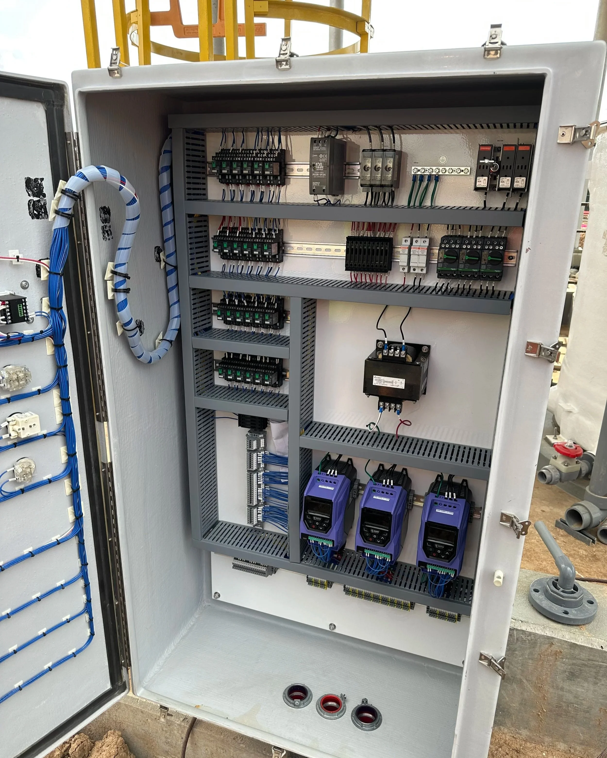 An electrical breaker panel with multiple switches, circuit breakers, and wiring organized on metal rails inside a gray metal box. The box is open, exposing the electrical components and wiring.