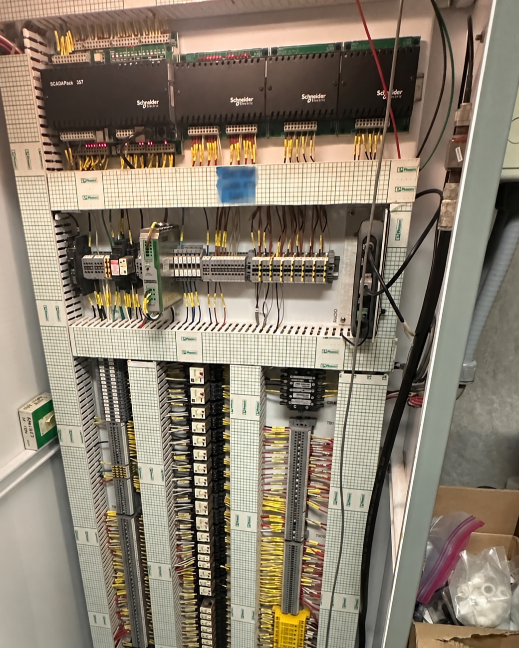 Electrical control panel with various terminals, relays, circuit breakers, and programmable logic controllers (PLCs) inside a metal enclosure.