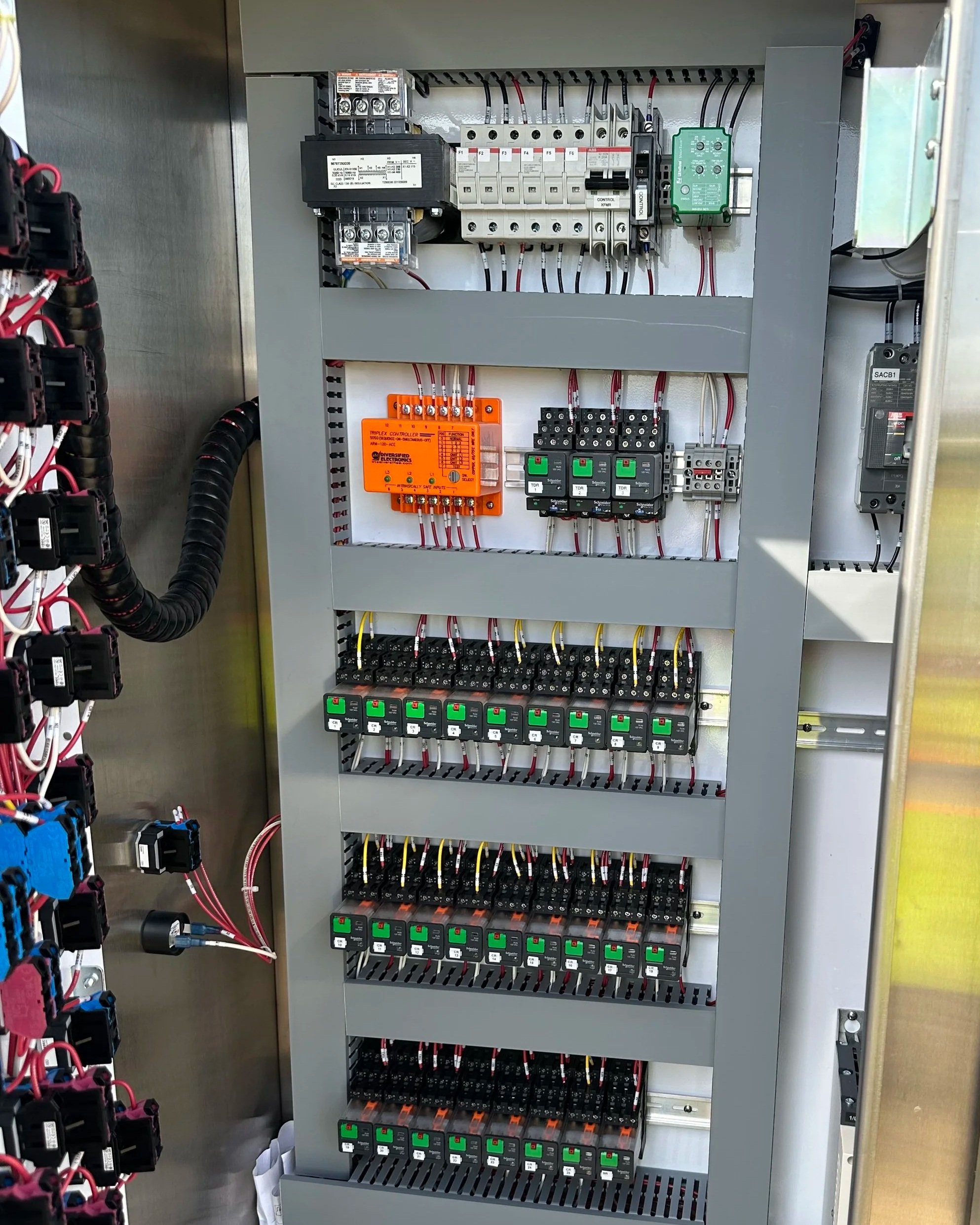 Electrical control panel with circuit breakers, relays, and wiring inside a metal enclosure.