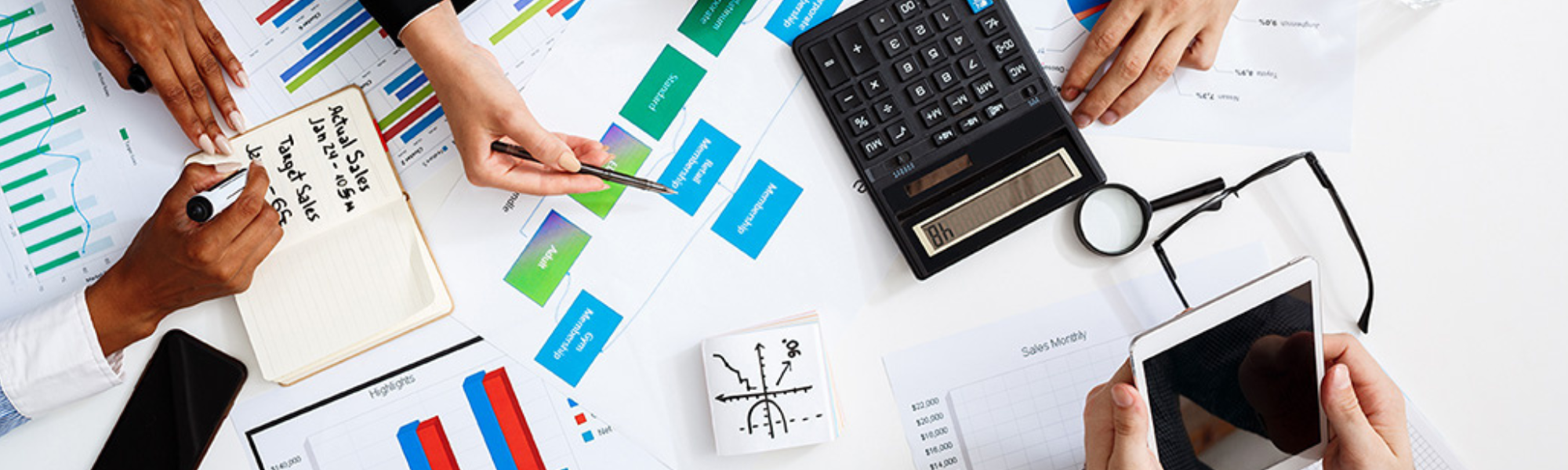 People analyzing financial and sales data with charts, graphs, a calculator, magnifying glass, and smartphone on a desk.