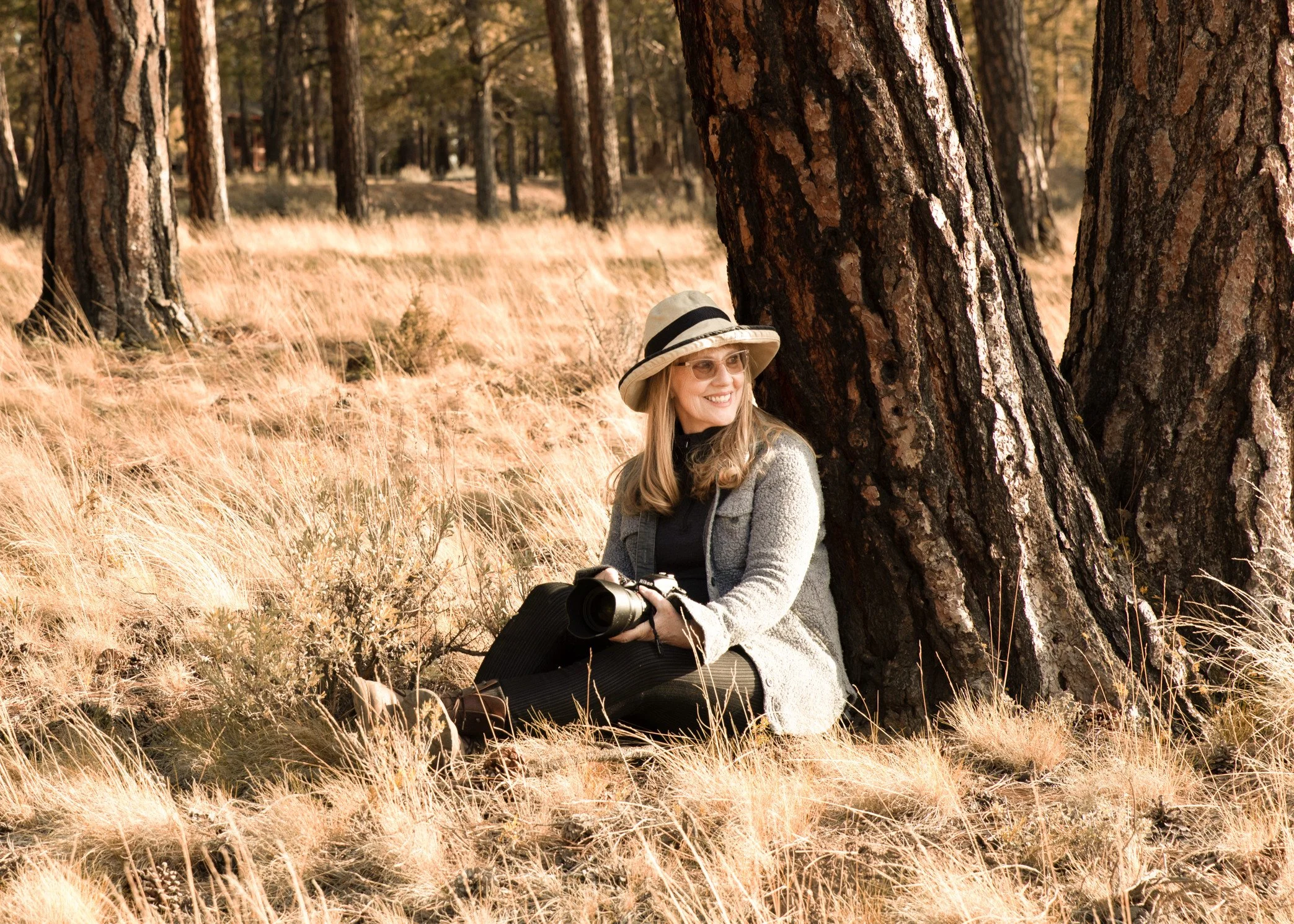 Local photographer seated beneath pine trees during an outdoor branding session in Central Oregon with camera in hand for website and marketing imagery.