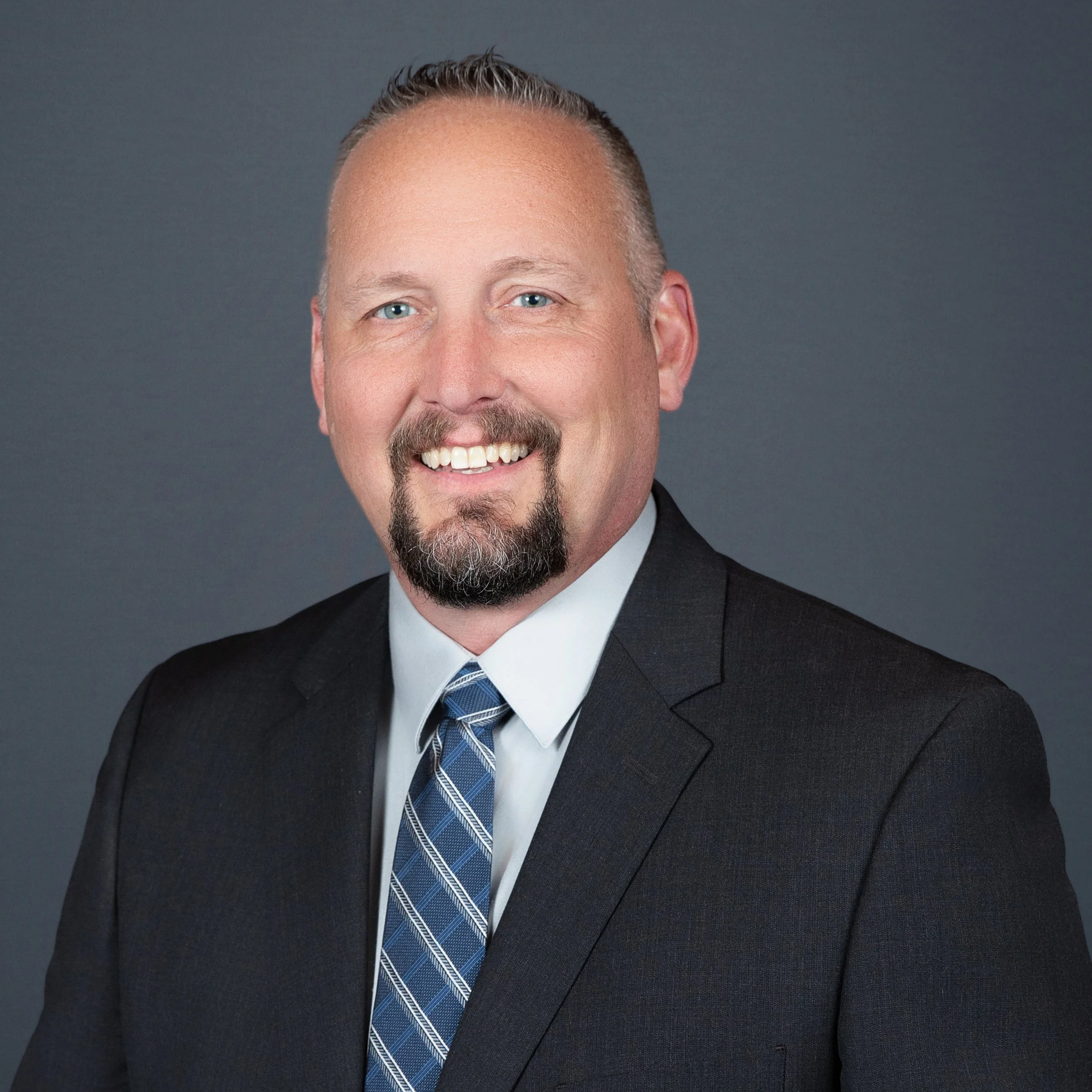 Professional business headshot of male executive in suit and tie with clean studio background