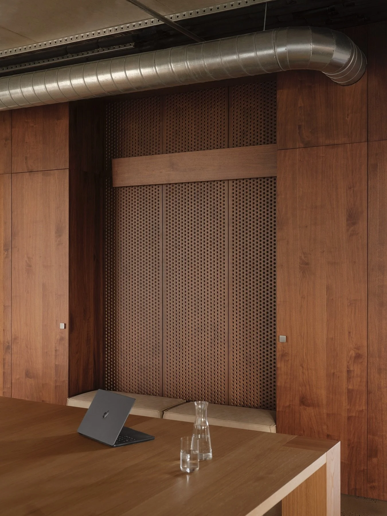 Detailed view of perforated walnut timber wall panels, integrated upholstered bench seating and exposed stainless steel ductwork at Programa HQ in Richmond.