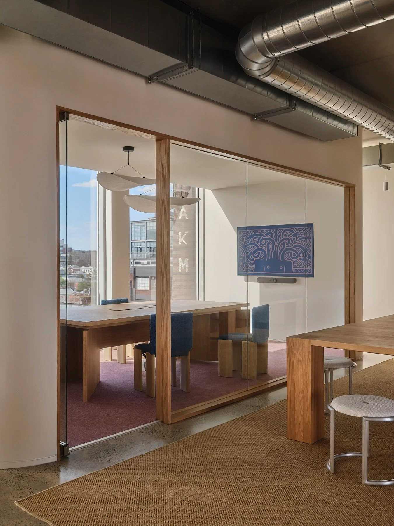 Custom American oak timber framed glass meeting room at Programa HQ with a custom American oak conference table, blue upholstered chairs, pink carpet and exposed metal ductwork.