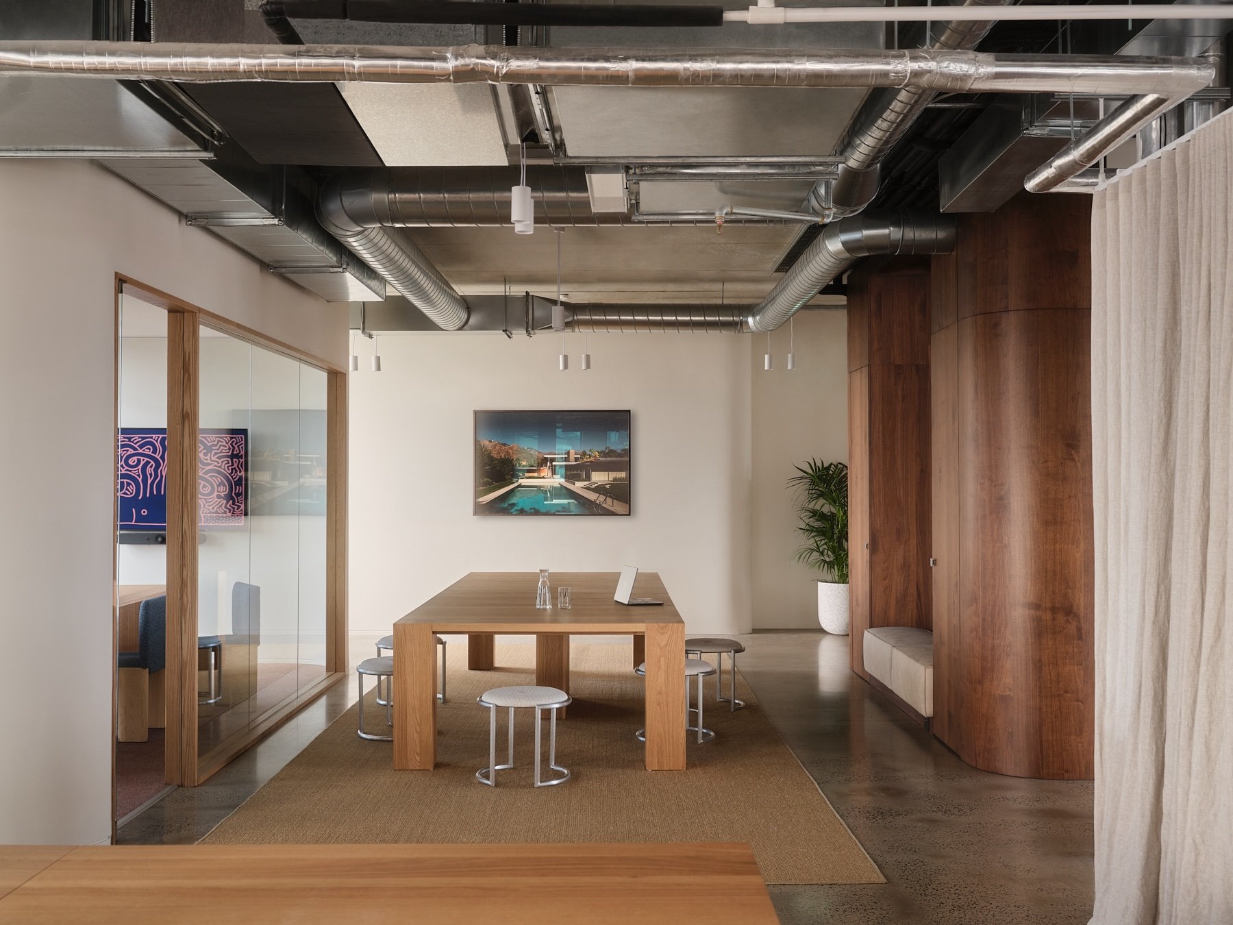 Wide architectural view of Programa HQ's shared meeting table, timber framed glass room, curved walnut joinery and exposed industrial ceiling in Richmond.