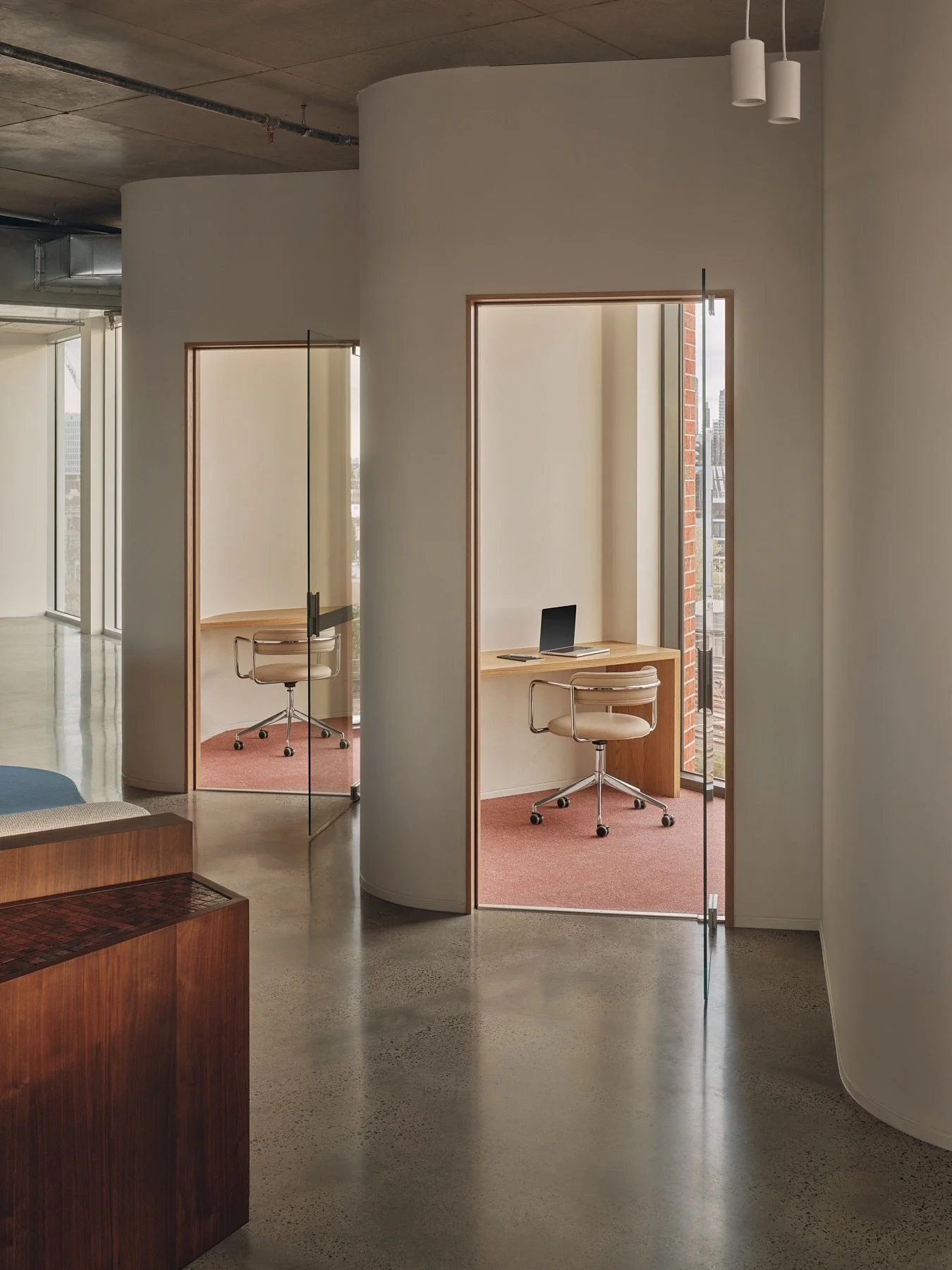Two curved private office pods at Programa HQ in Richmond with timber-framed glass doors, custom desks, cream swivel chairs and pink carpet.