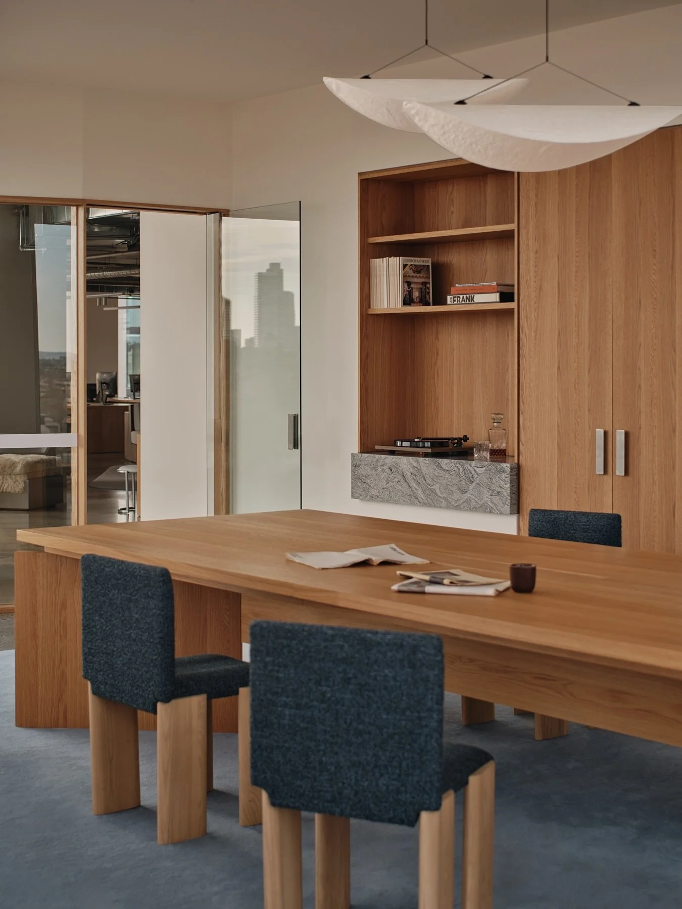 Programa HQ boardroom with a large custom timber table, blue upholstered timber chairs, built-in shelving, stone shelf detail and suspended white pendant lights.