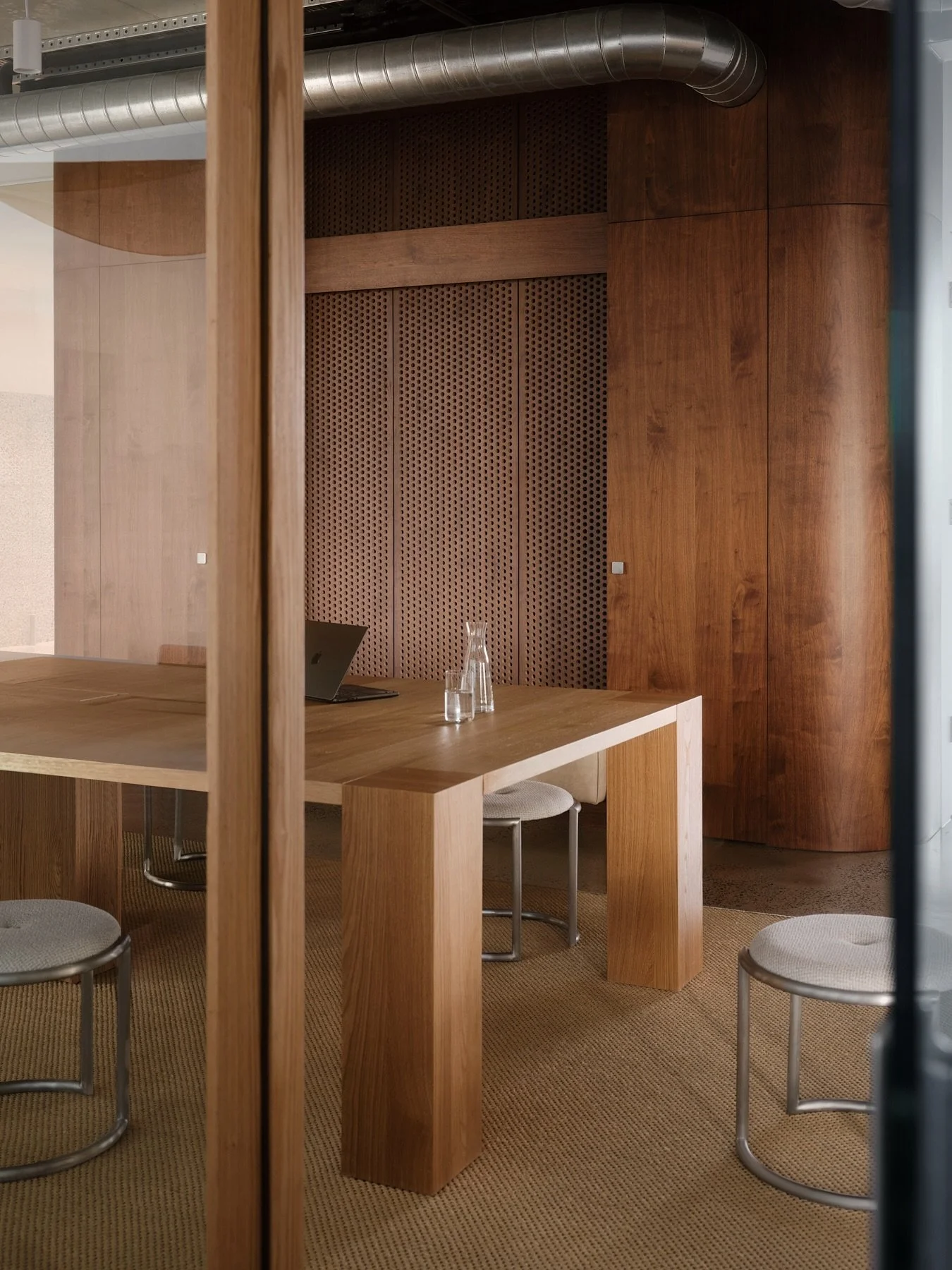 Close architectural view of a custom solid timber meeting table, upholstered metal stools and curved perforated timber wall at Programa HQ in Richmond.