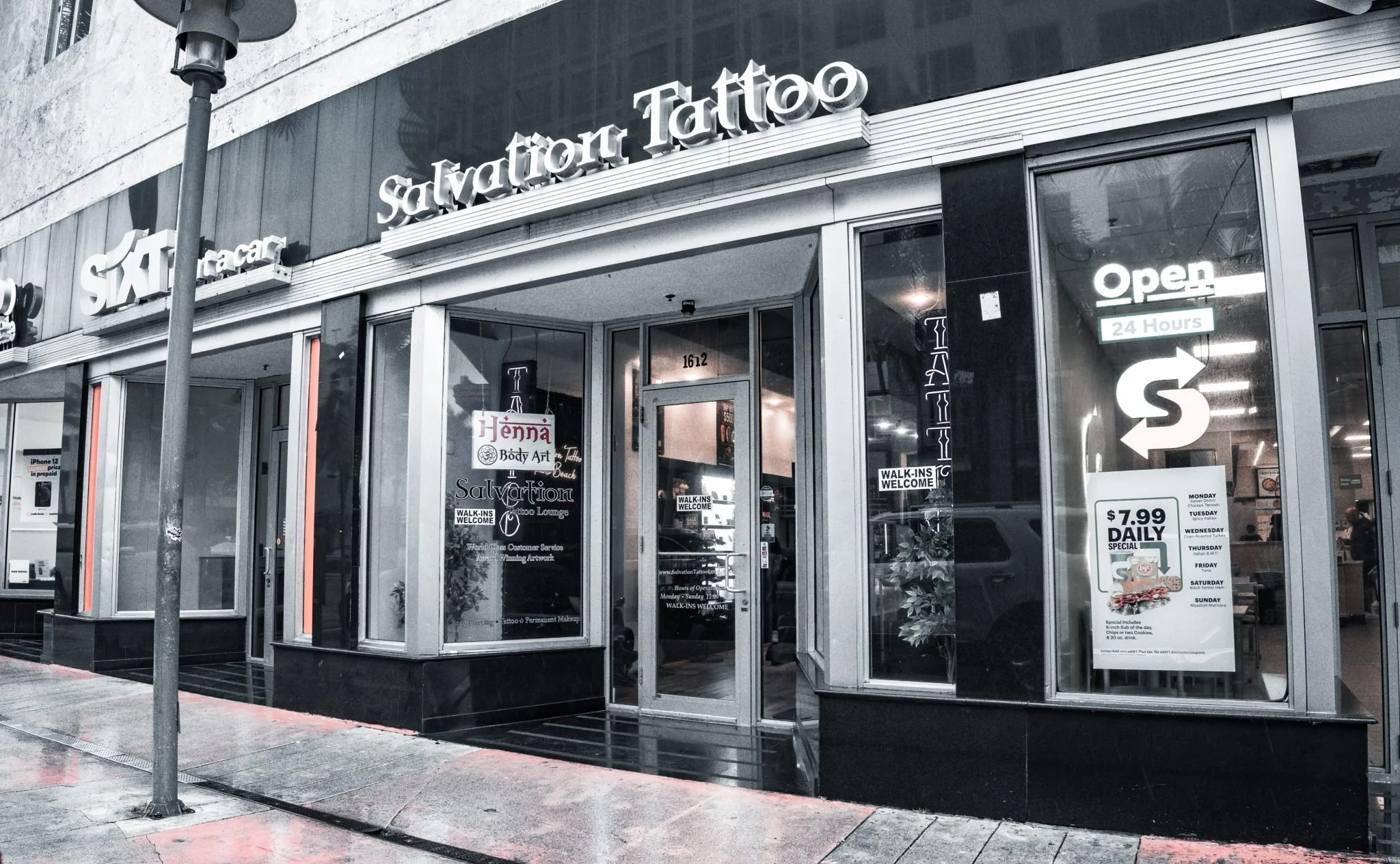 “Interior of Salvation Tattoo Lounge in Miami Beach featuring professional tattoo stations, artists at work, and retail merchandise.”