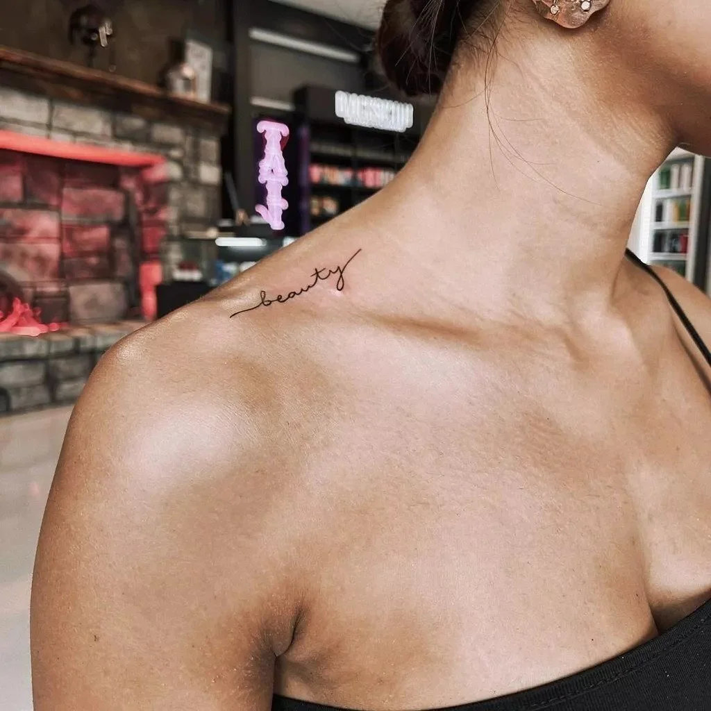 Small fine-line script tattoo placed along the collarbone with delicate lettering