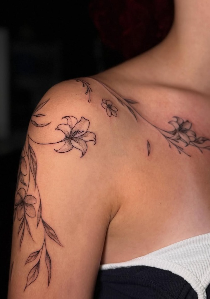 Delicate fine-line floral shoulder tattoo with flowers and leaves by Carol