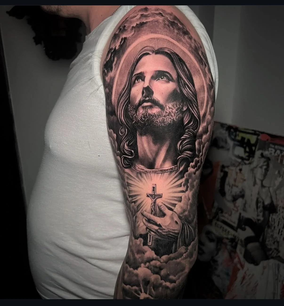 Black and gray realism sleeve tattoo depicting Jesus with detailed shading, clouds, and religious symbolism