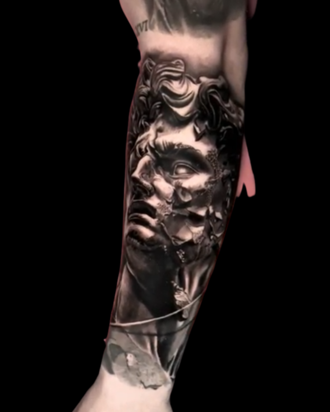 Black and gray realism forearm tattoo of a fragmented classical statue face with dramatic shading.