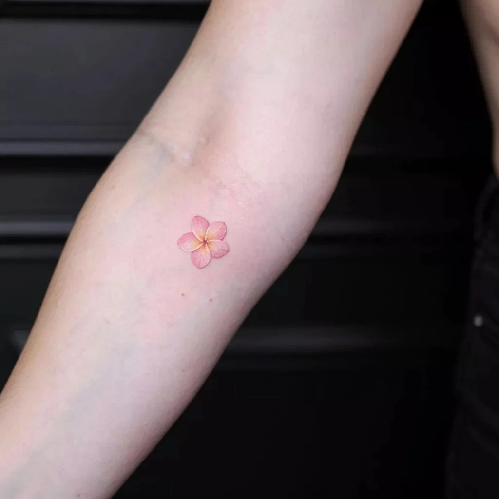 Minimal fine line flower tattoo on the inner arm with subtle pastel details