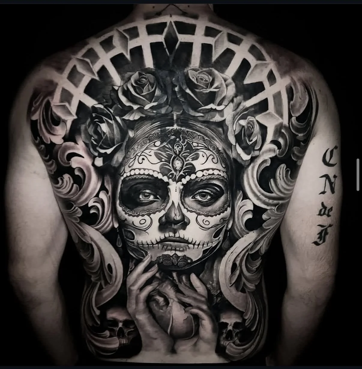 Black and gray realism full back tattoo featuring a detailed sugar skull portrait with roses and ornamental elements
