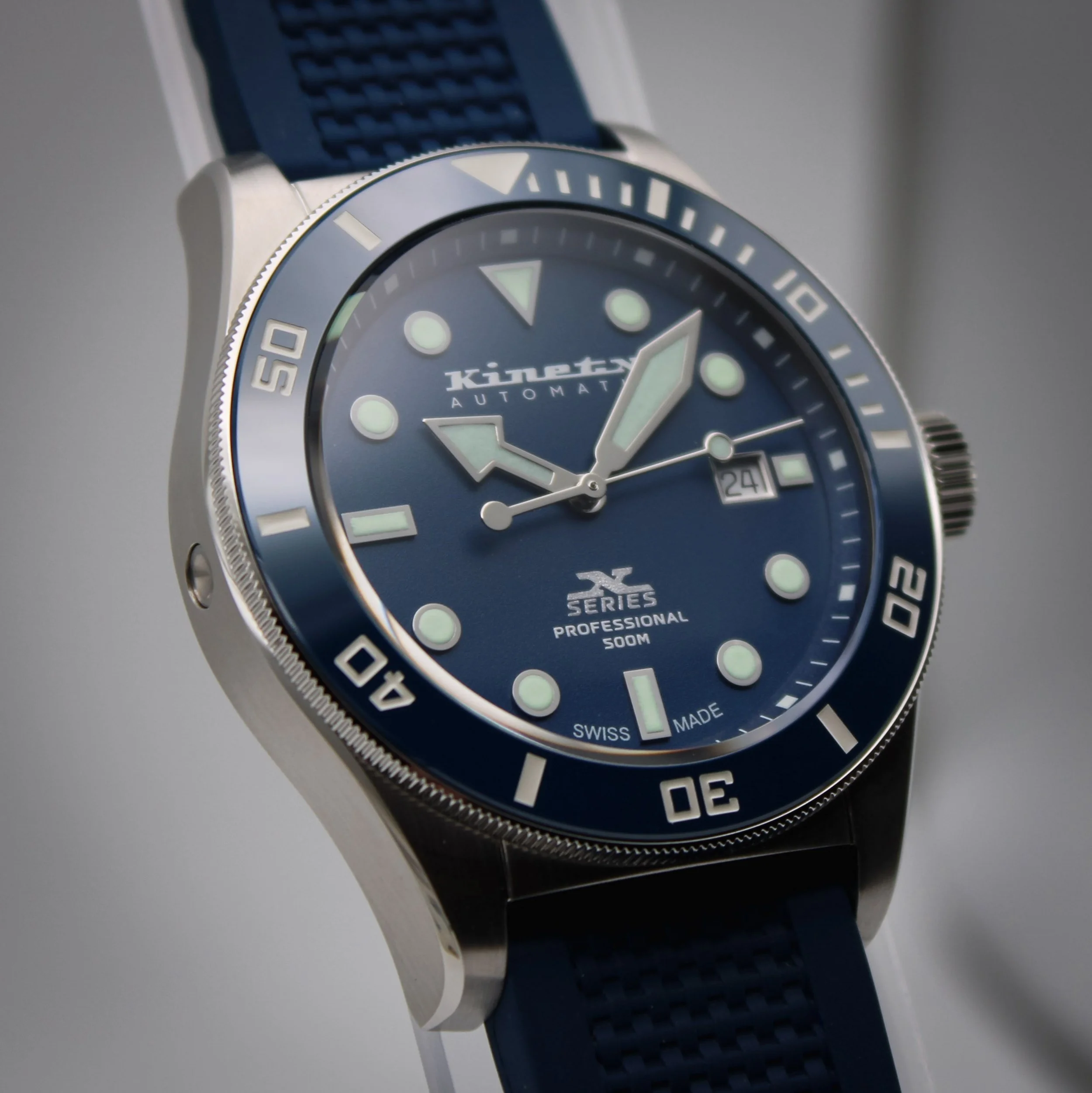 Close-up of a Kinetix X Series analog watch with a stainless steel band, featuring a black dial, white markers, and a date window.