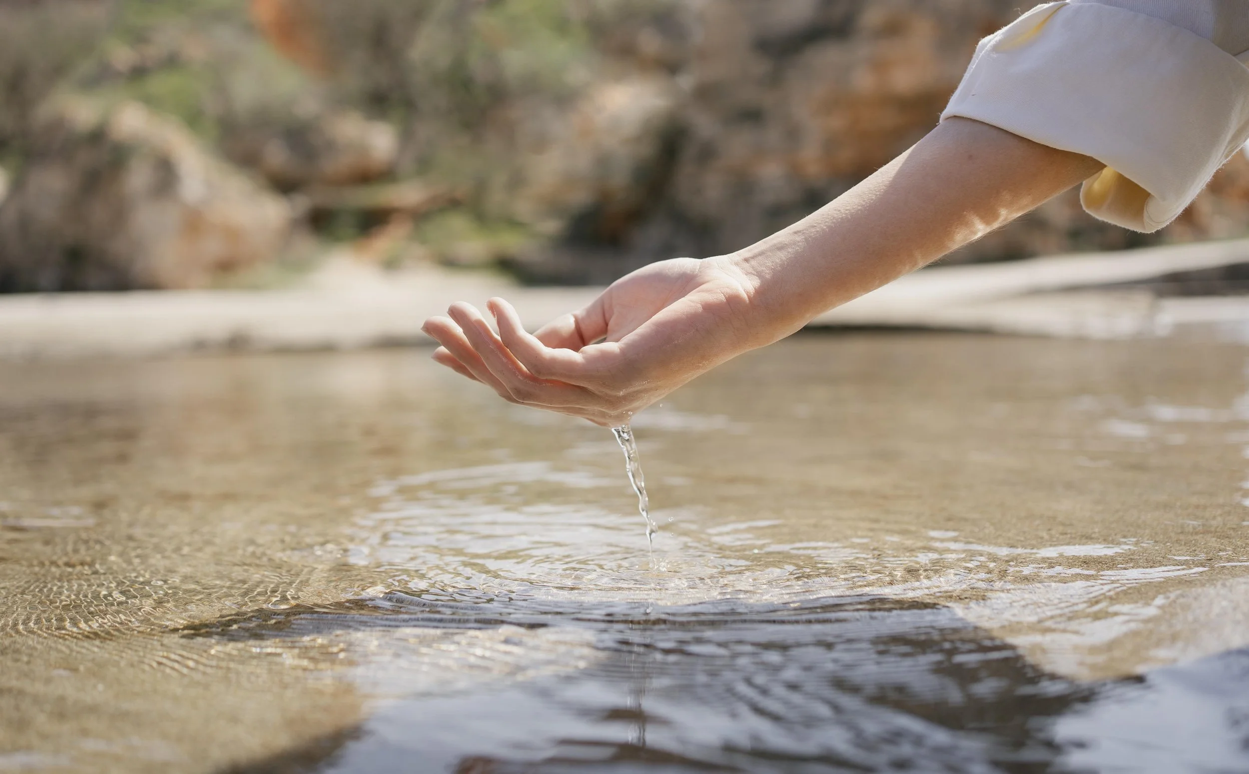 A person reaching out their hand to touch water in a natural setting