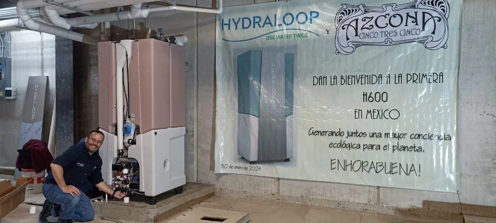 A man installing a water treatment system in front of a banner that reads 'Hydraloop'.