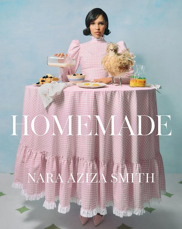 Nara Smith wearing a pink gingham dress that fits perfectly over a round tabletop with food displayed