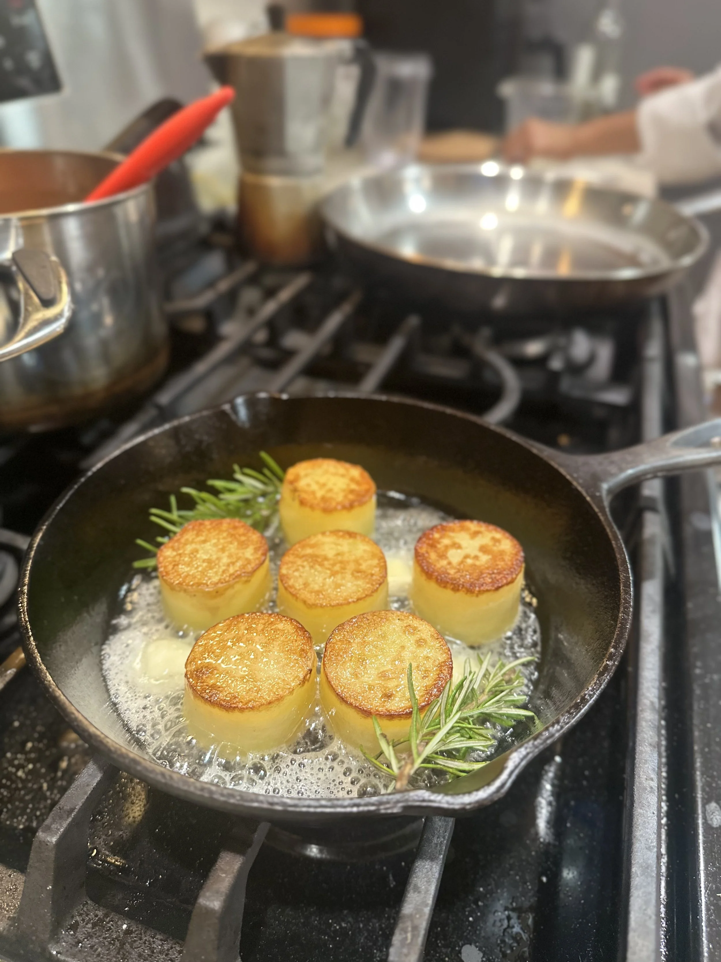 Fondant potatoes  in a pan with garlic and herbs, garnished with a sprig of rosemary.