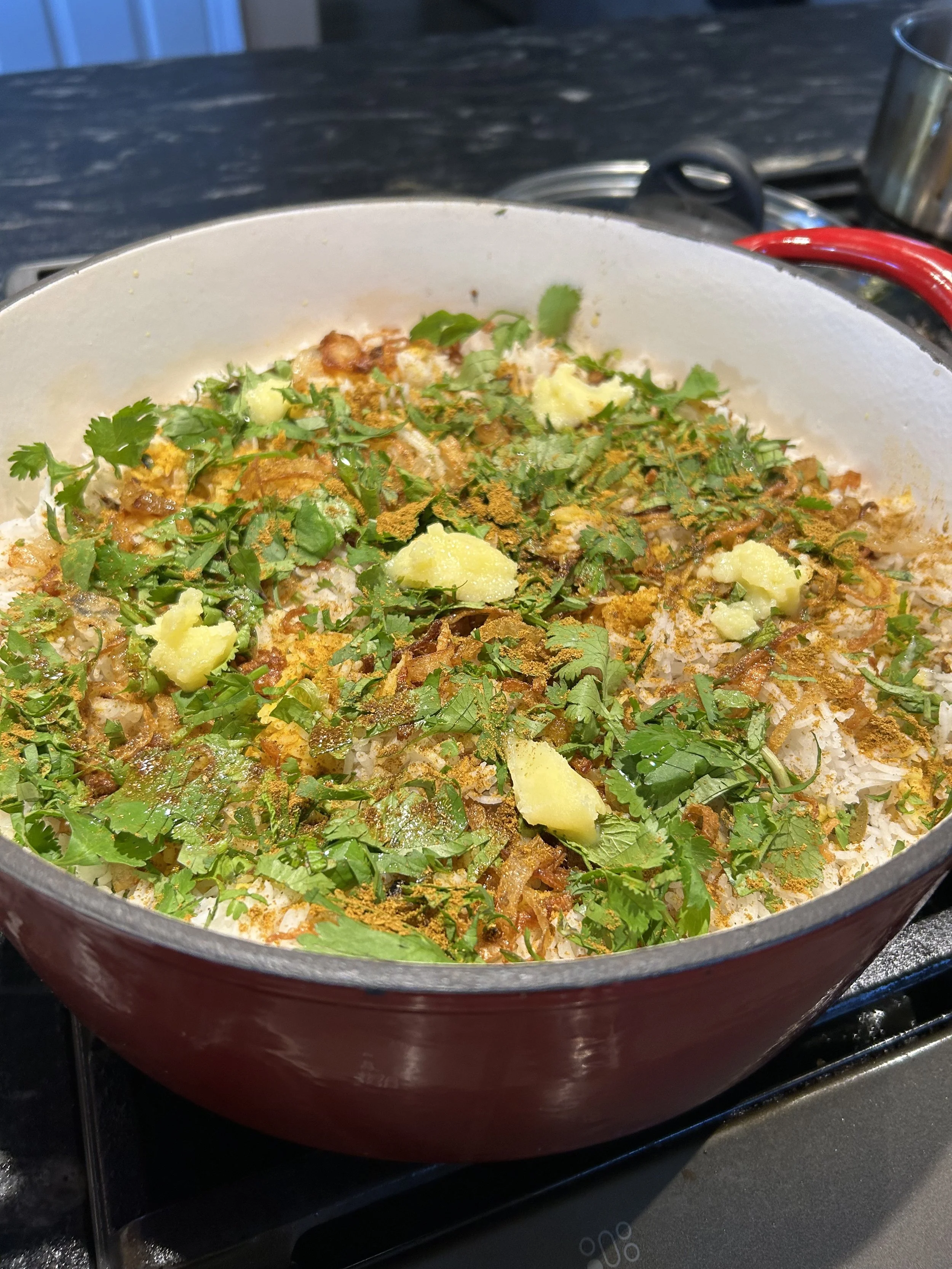 A cooked dish in a red cast iron skillet, topped with chopped cilantro, pieces of potatoes, and spices.