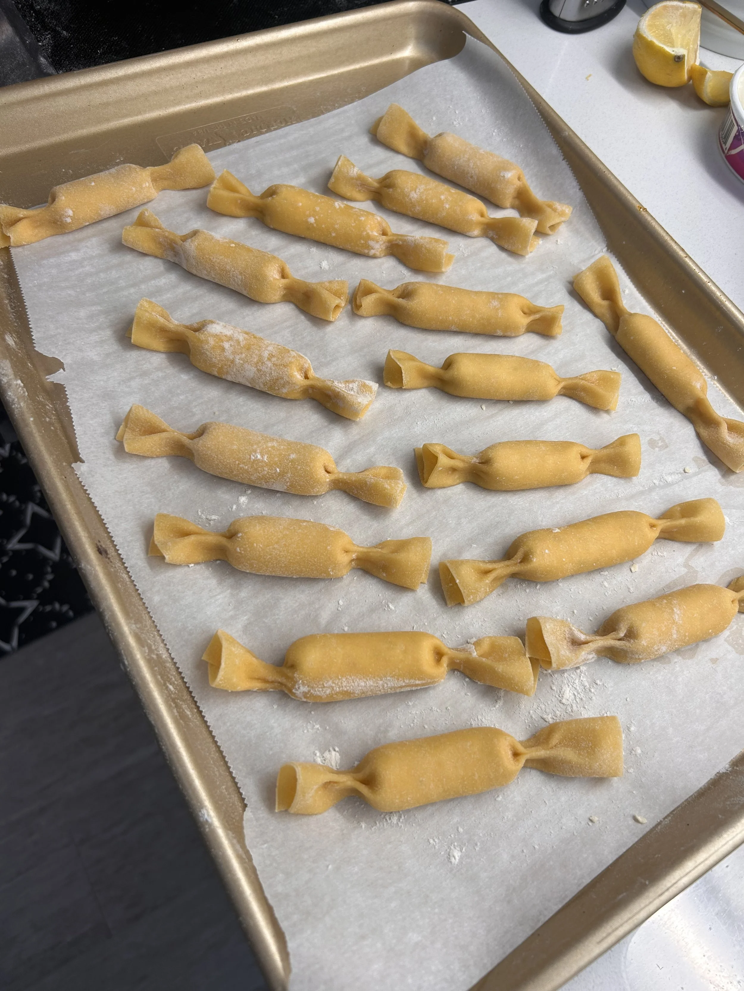 Unbaked tortellini pasta on a baking sheet lined with parchment paper, with lemon wedges and a container in the background.