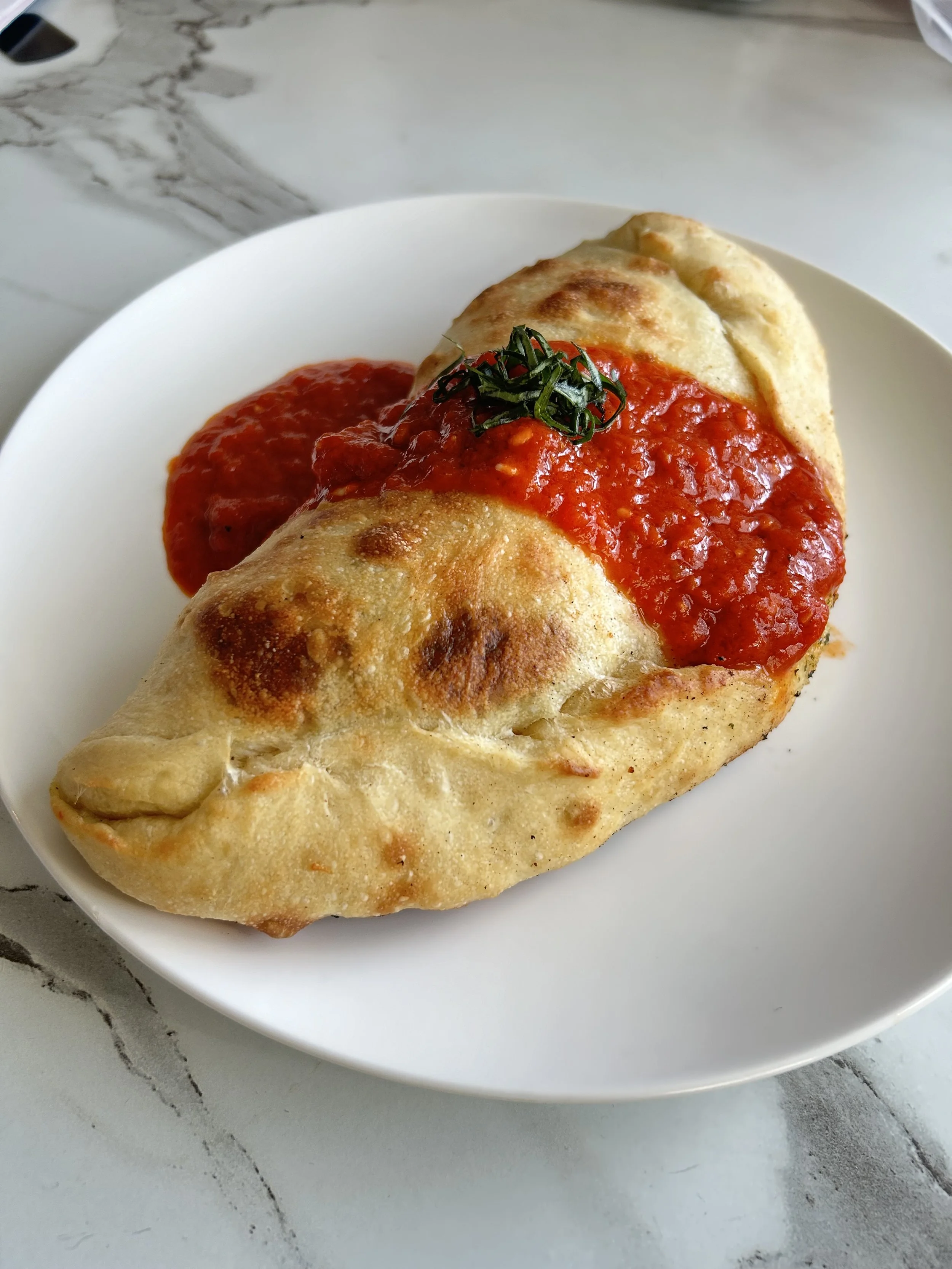 Calzone with marinara sauce and basil on a white plate.
