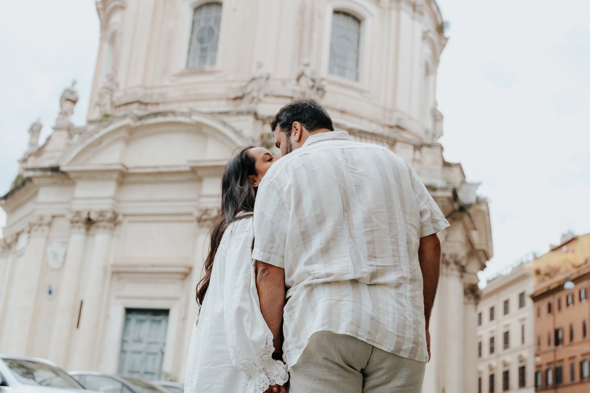 A couple kissing in front of an ornate historic building in the heart of Rome.