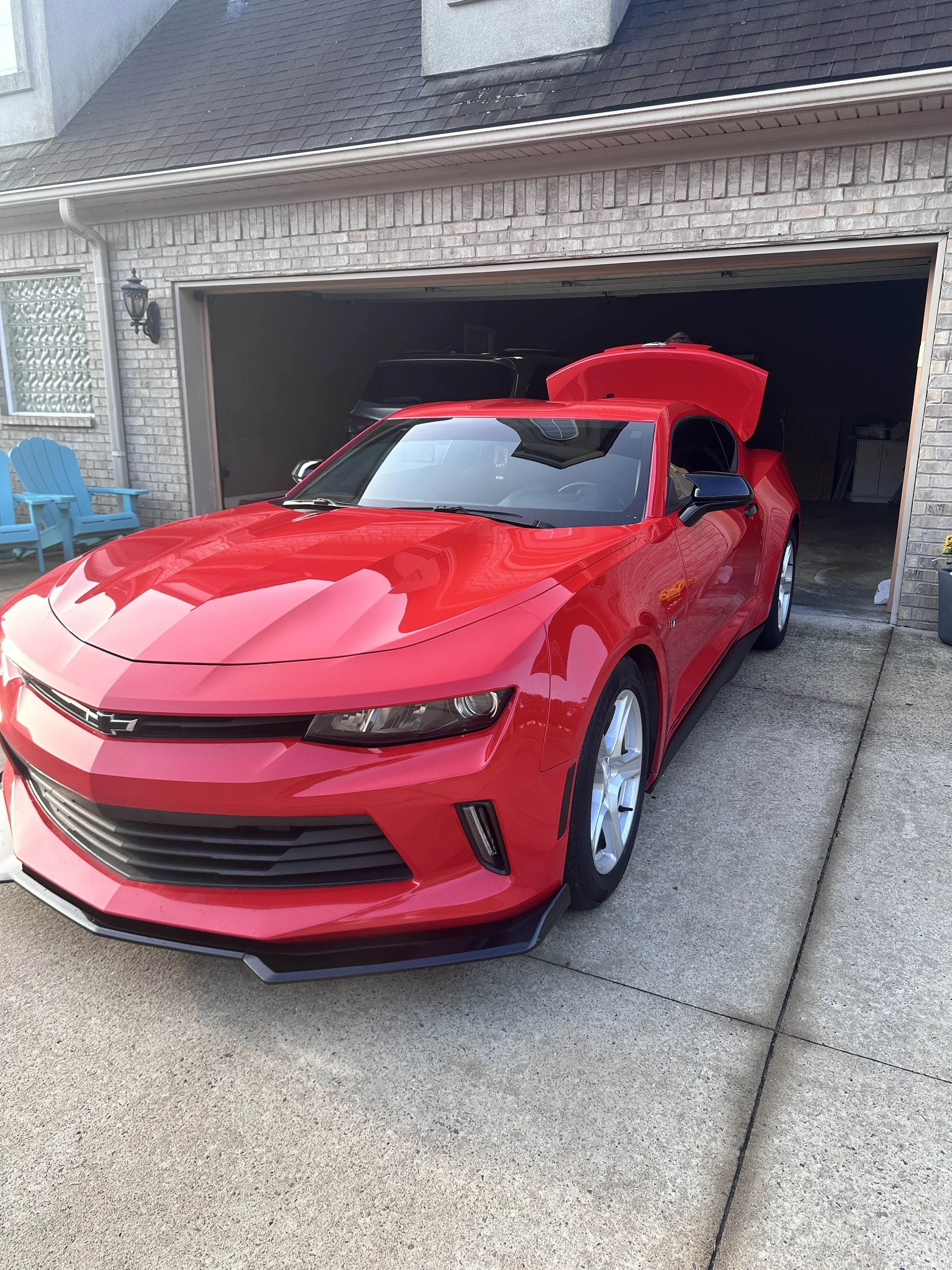 Red Chevrolet car parked in front of a garage with the hood open.