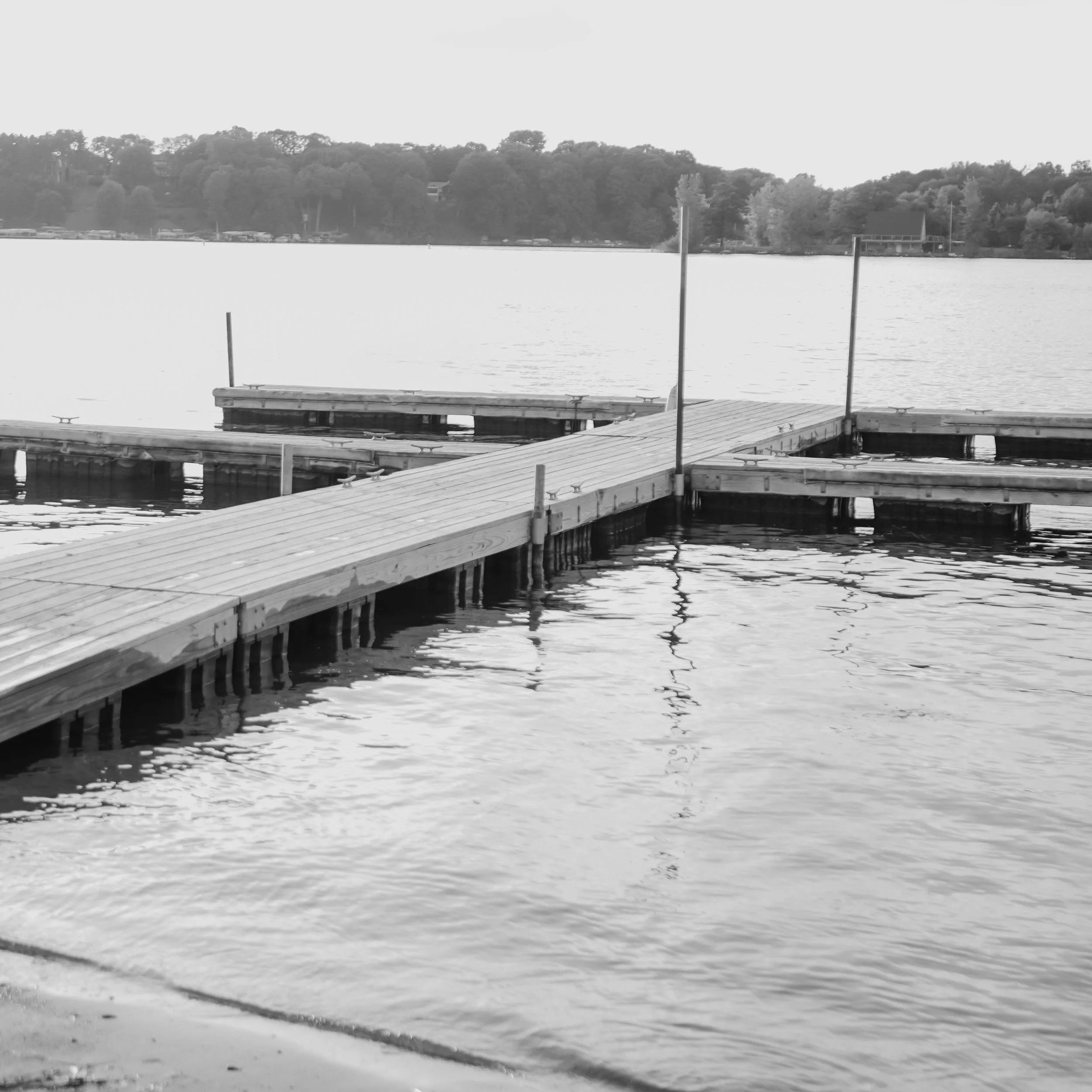 Black and white photo of a wooden dock extending into a body of water with trees in the background.