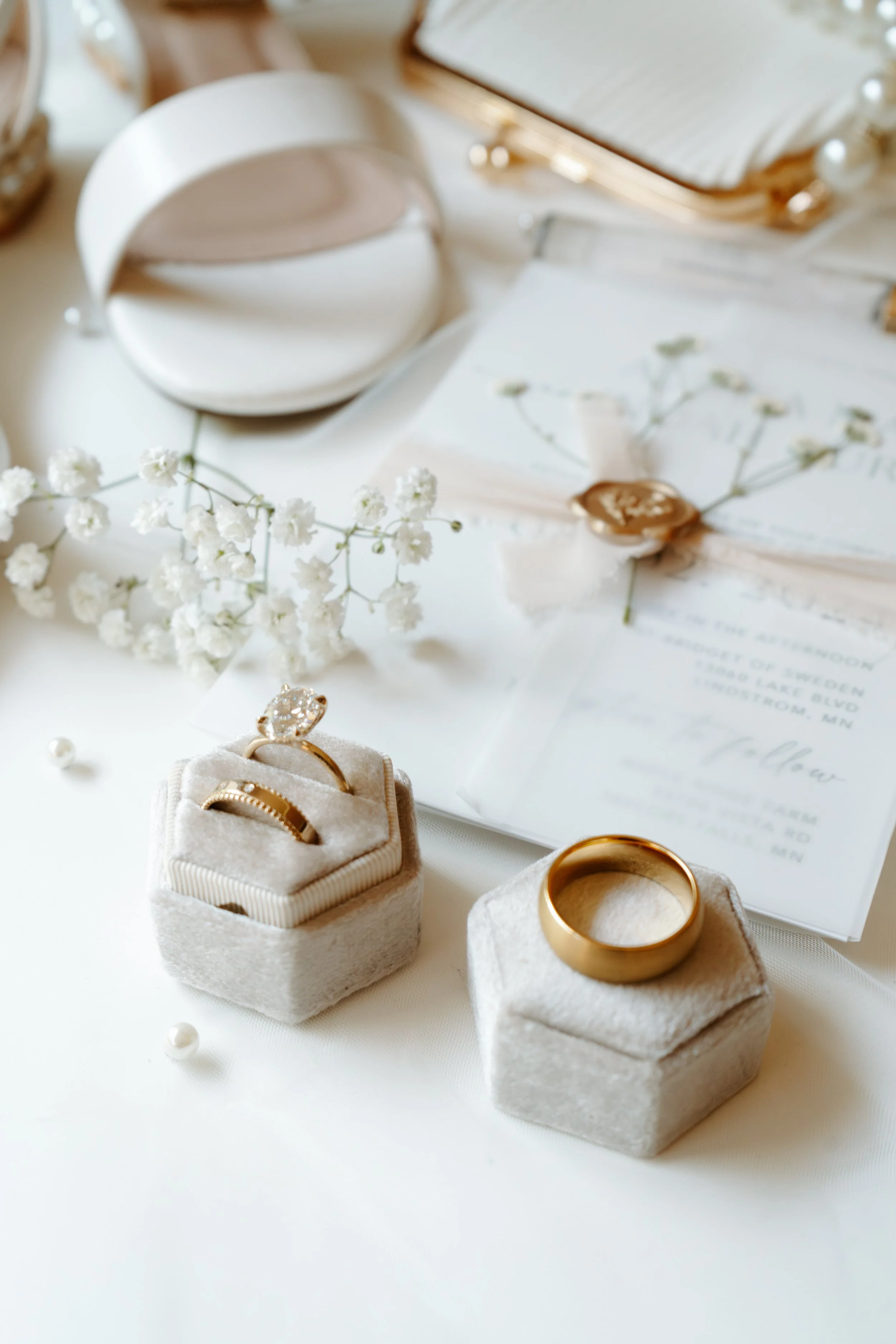Close-up of wedding rings, one with a diamond, in velvet rings boxes, on a table with flower decorations and a wedding invitation.