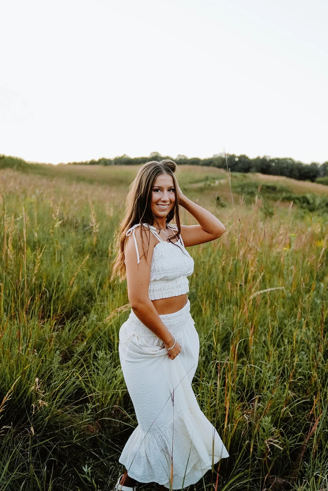 Young woman standing in a grassy field during sunset.