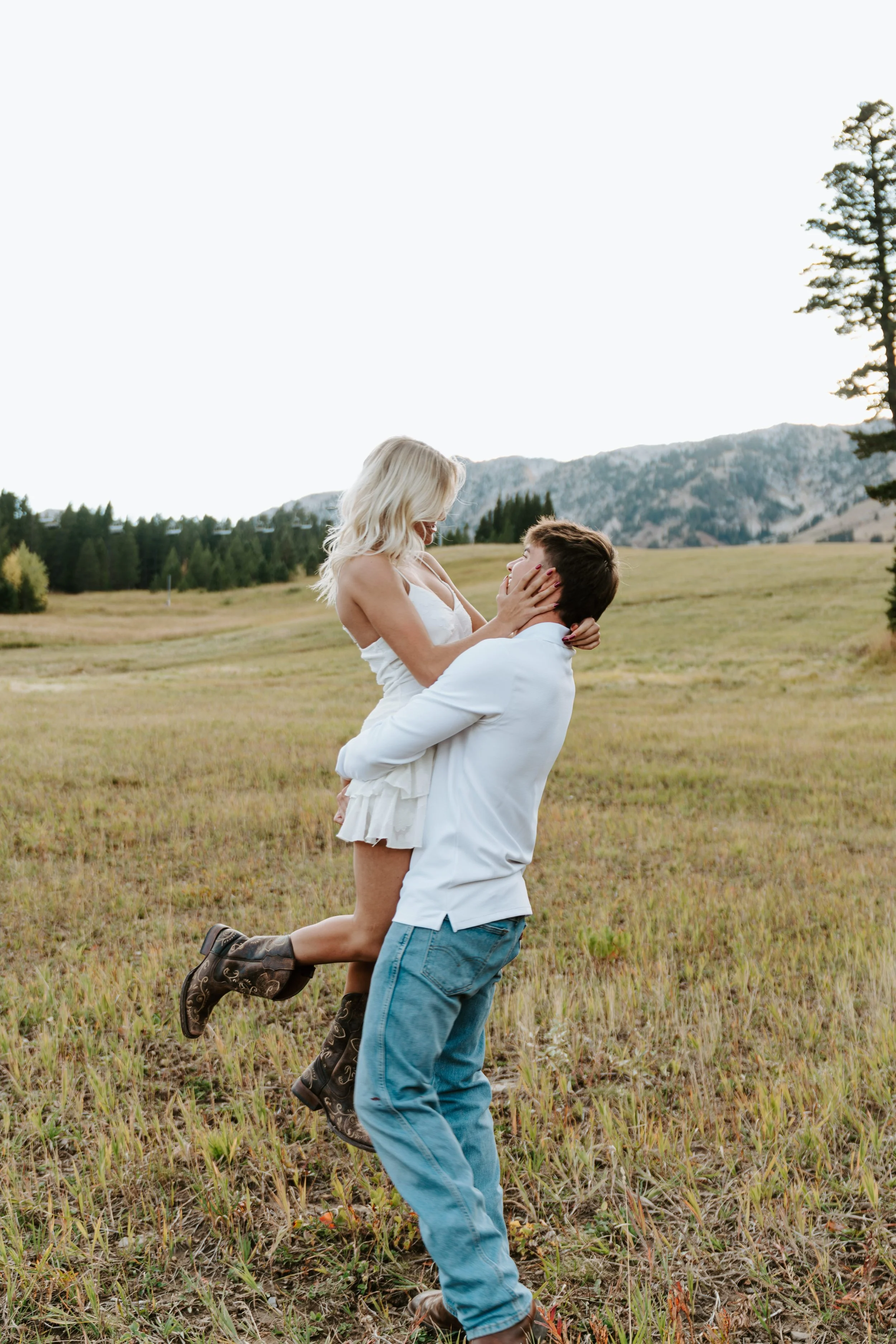 A man lifting a woman in a field with mountains in the background.