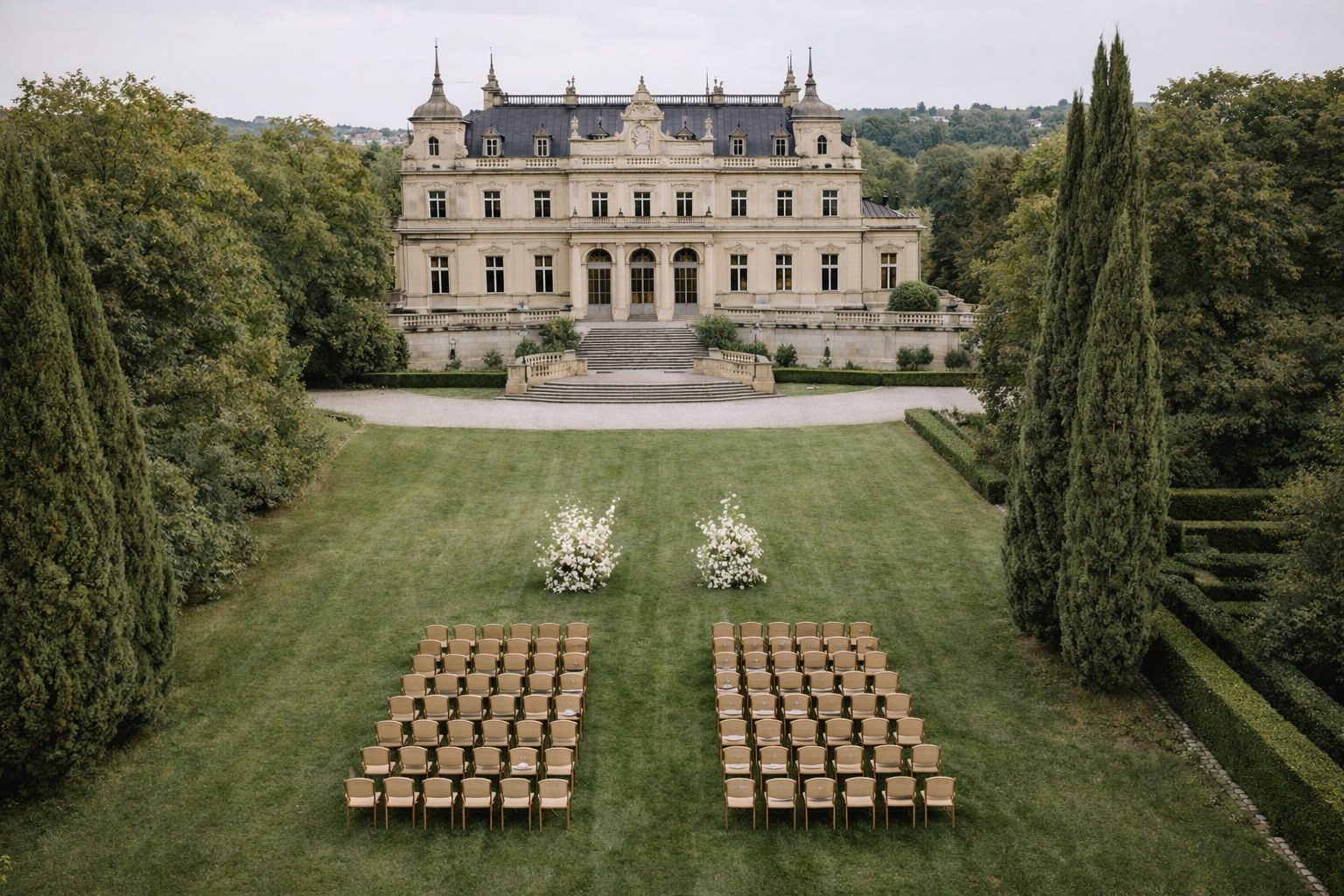 Eleganter Garten mit Stuhlreihen für eine Veranstaltung vor einem historischen Schloss, mit Bäumen und Blumen im Hintergrund.