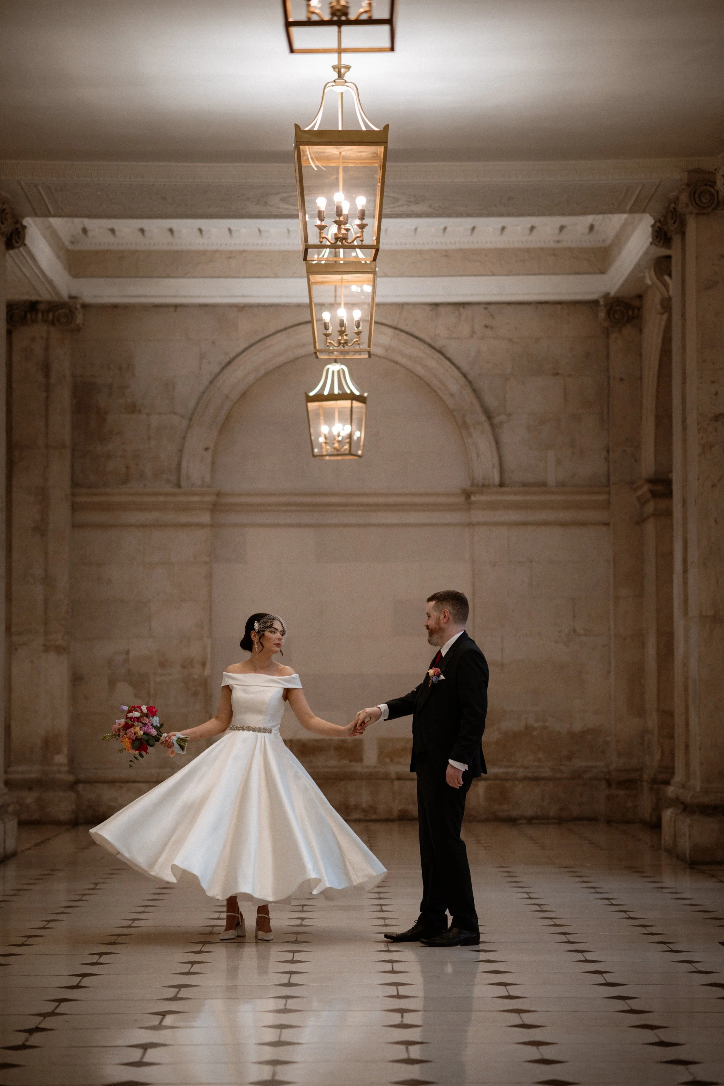 Bride and groom in elegant hallway of Dublin City Hall , bride holding bouquet, vintage lighting overhead.