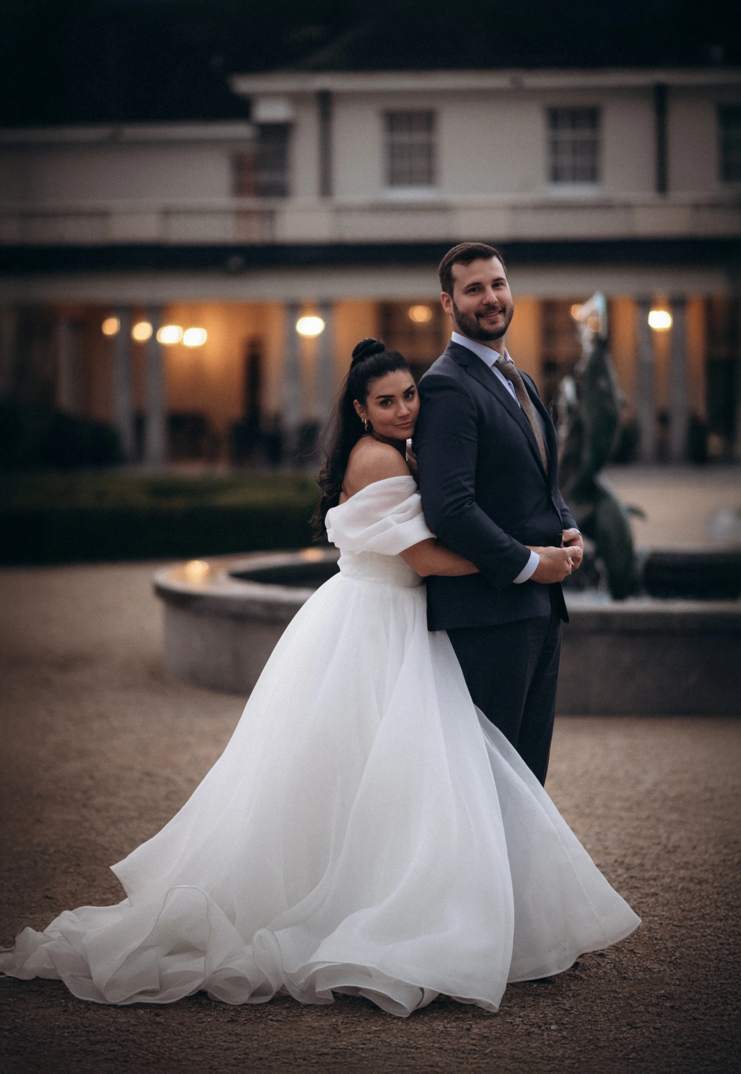 Bride in white gown hugging groom in suit in front of CastleMartyr Hotel