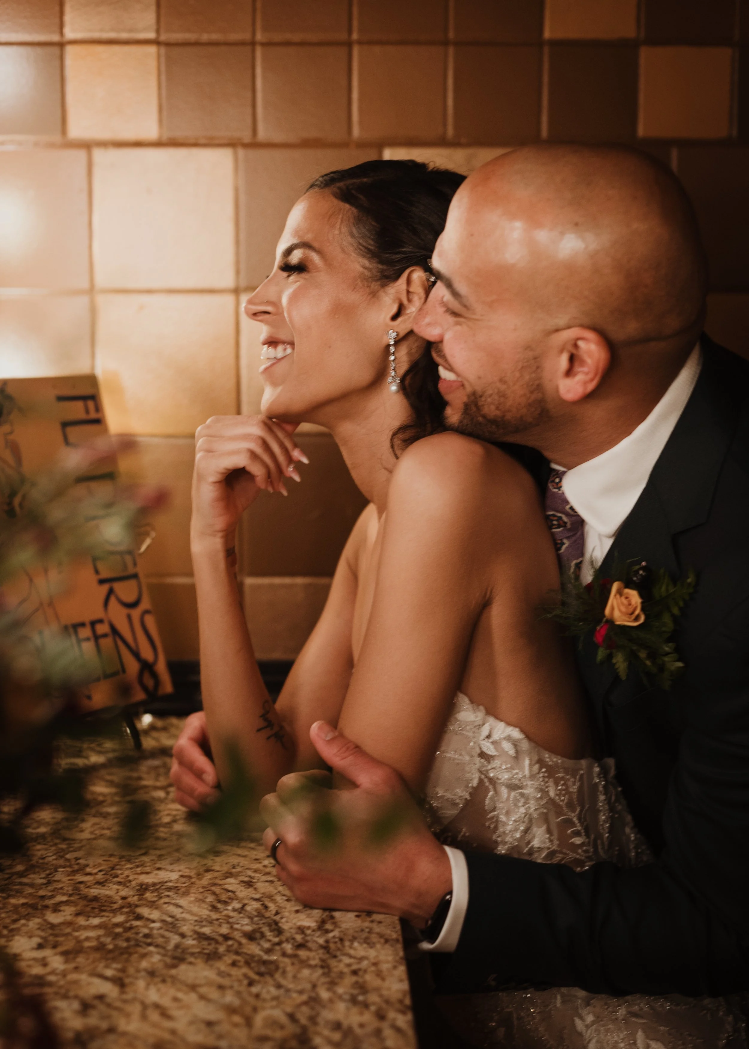 Bride and groom share a joyful, intimate moment at their wedding reception. She leans back, laughing as he embraces her from behind. Warm golden light and soft details create a romantic ambiance. Captured by a Seattle wedding photographer.