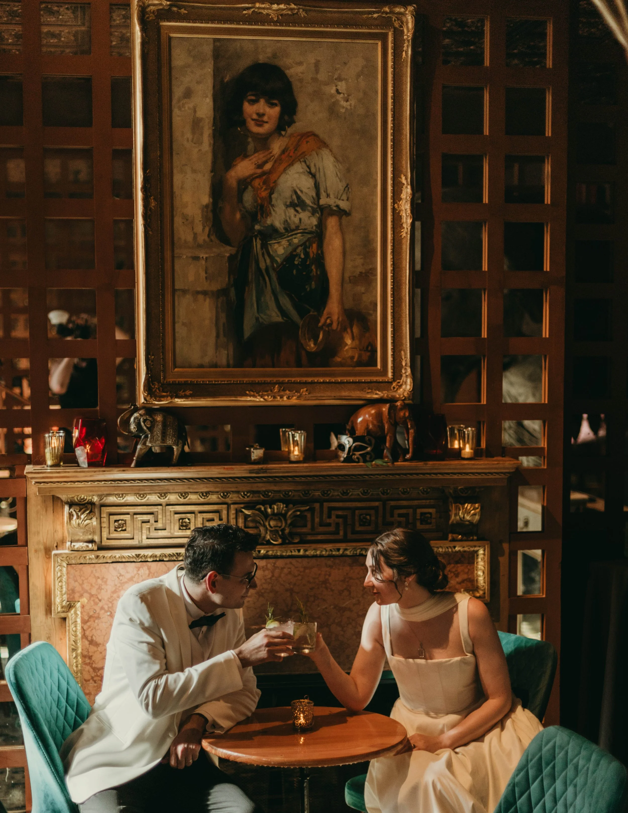 Bride and groom share a toast in an intimate, vintage-style lounge with warm candlelight. An ornate fireplace and a large oil painting set the romantic, moody atmosphere. Captured by a Seattle wedding photographer.