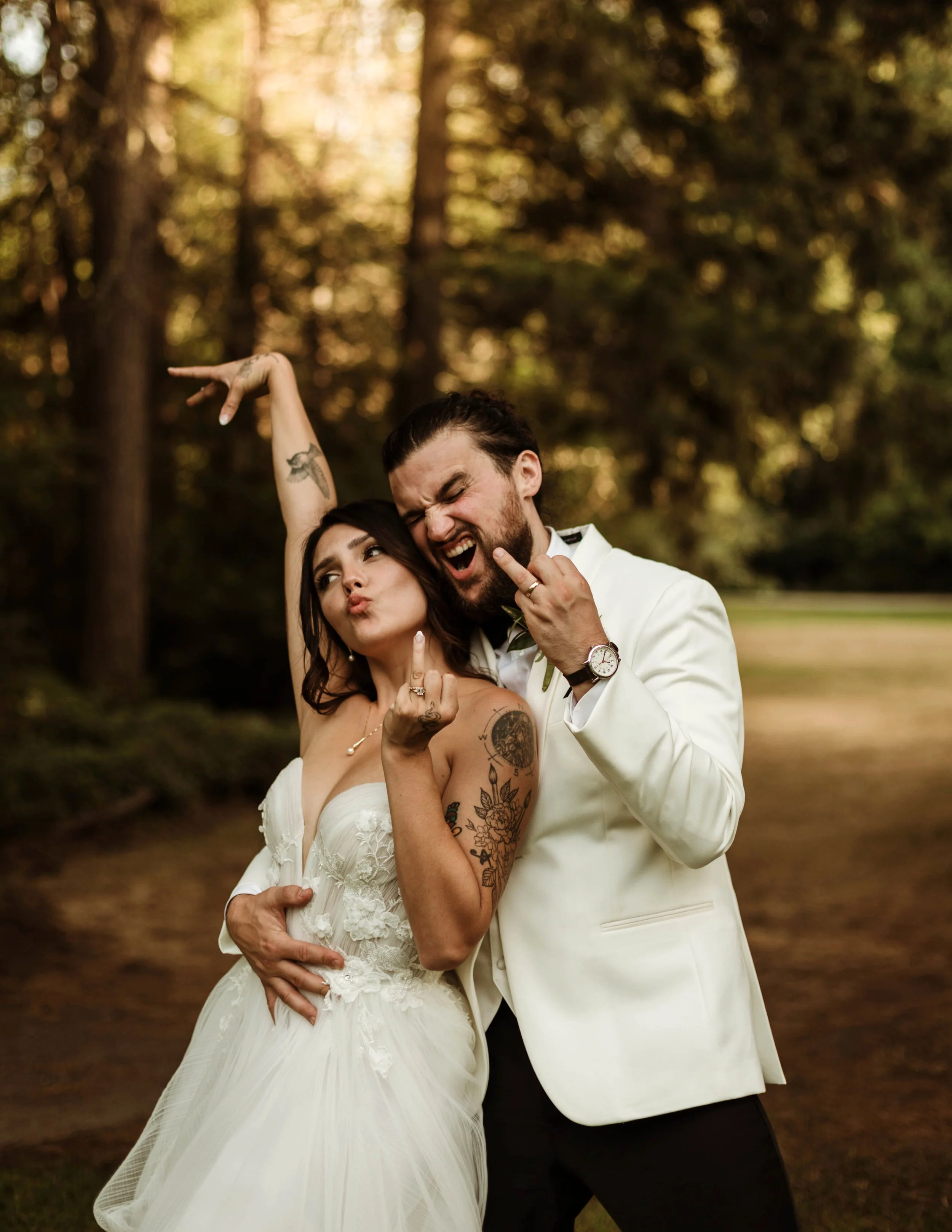 Tattooed bride and groom celebrate their wedding with playful, rebellious energy. She strikes a pose while he flashes a grin, both showing off their rings. A bold and unconventional wedding moment captured by a Seattle wedding photographer.