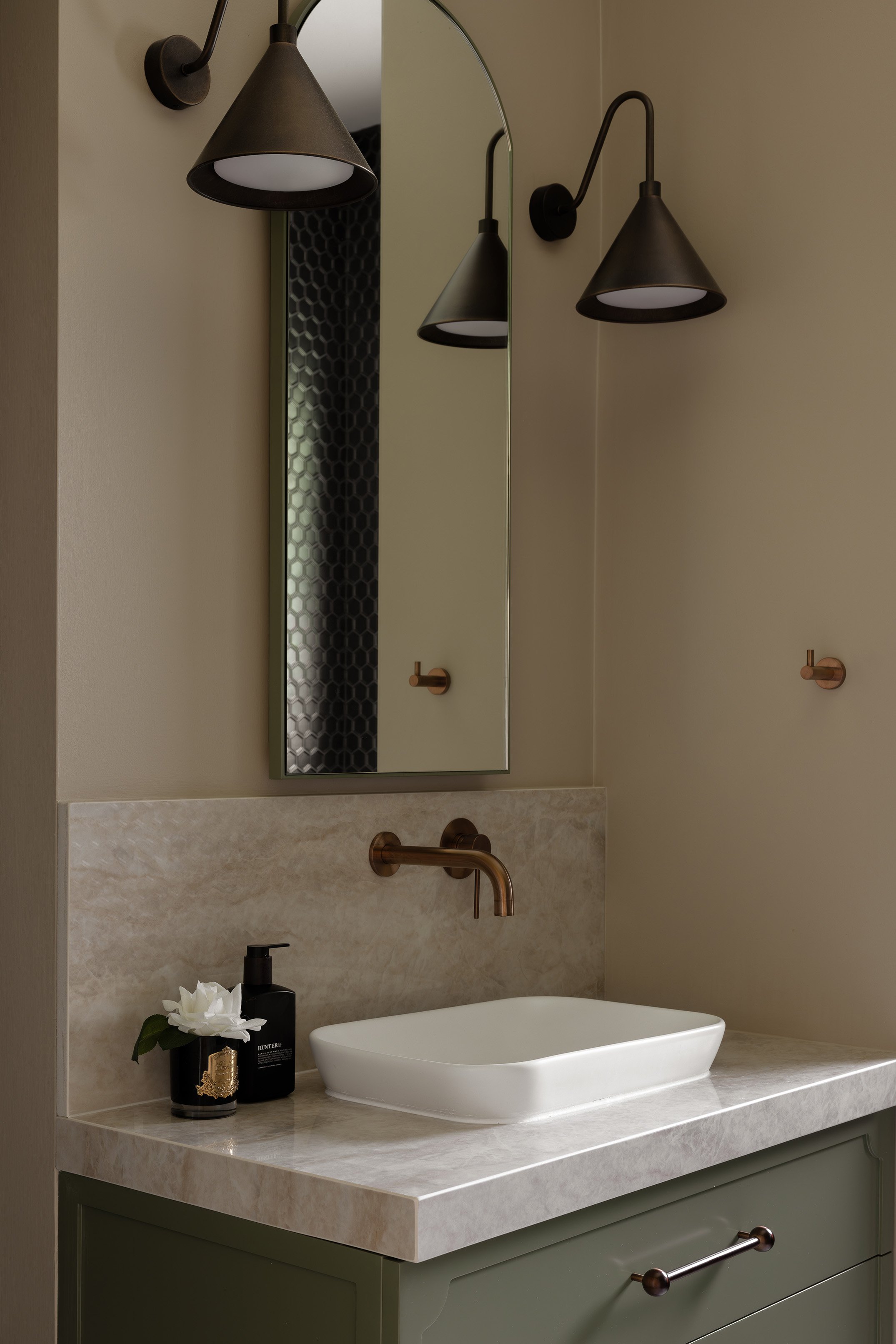 Bathroom vanity with a rectangular vessel sink, black soap dispenser, decorative flower, and two wall-mounted light fixtures above a mirror.