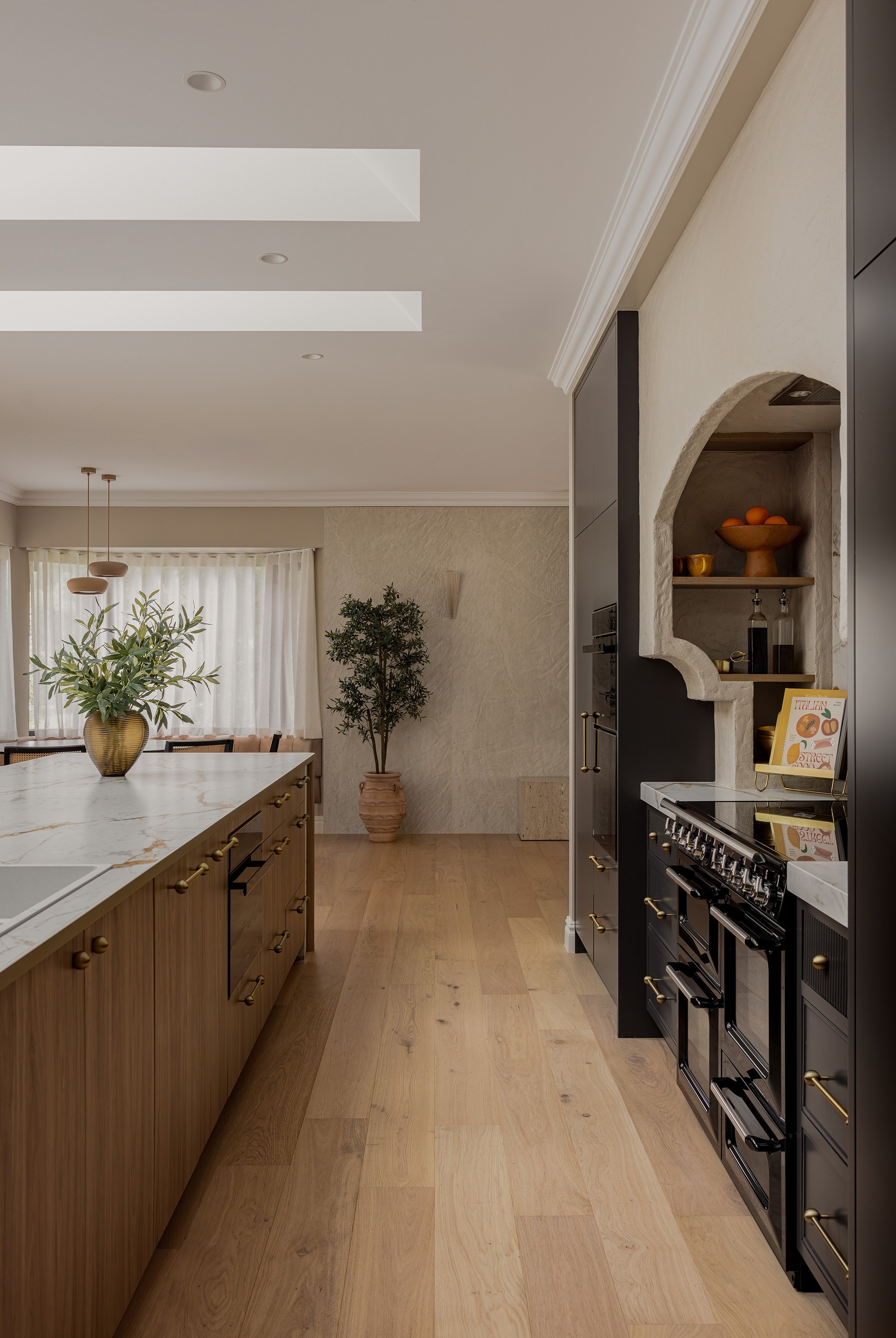 Modern kitchen with wooden island and black oven, open shelves with bowls and bottles, and potted plants in the background.