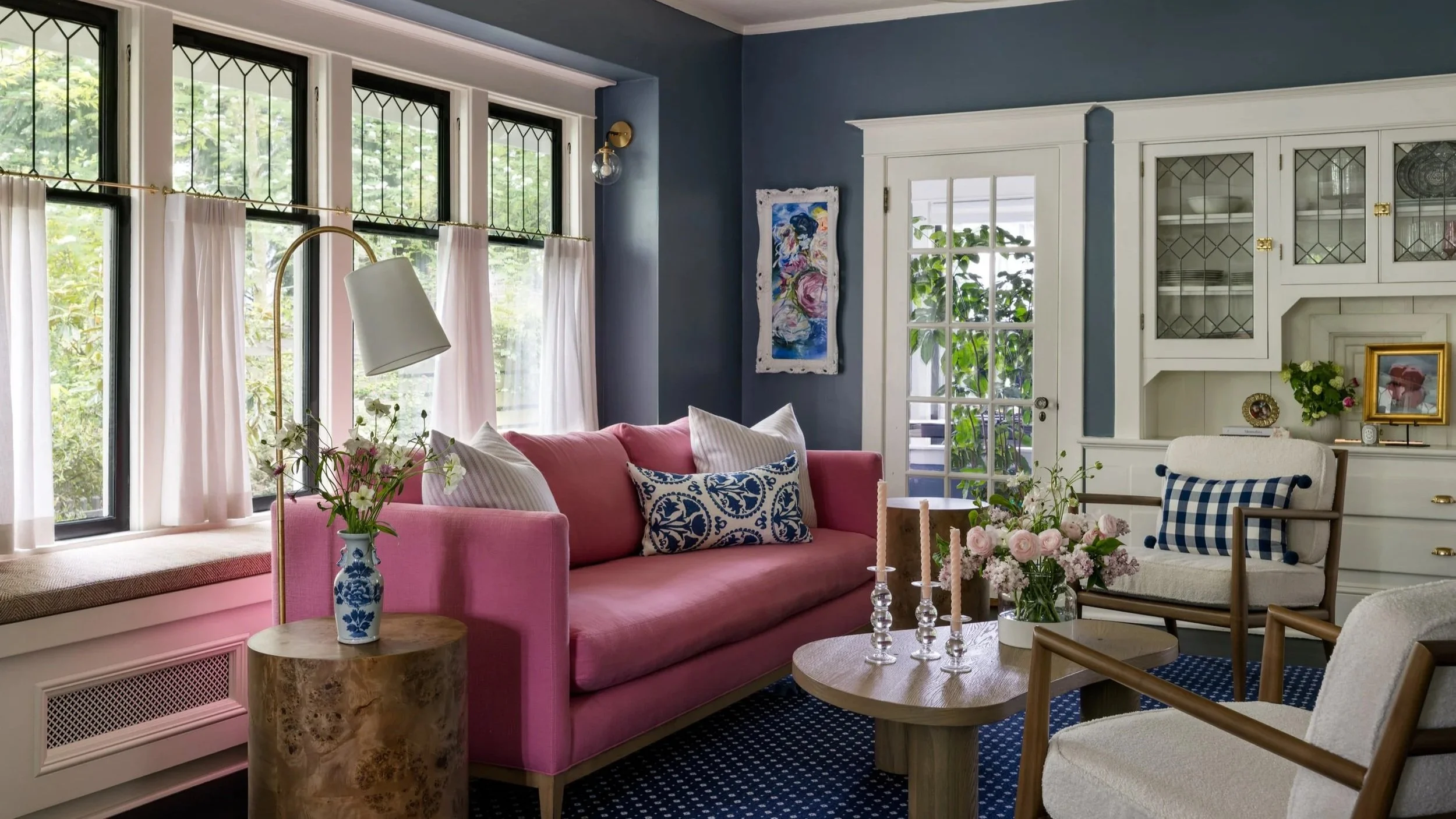 A vibrant, welcoming interior that supports daily life while celebrating the home’s original architectural charm. A tailored pink sofa in the living room, complemented by patterned blue textiles, sculptural wood tables, and vintage-inspired lighting 