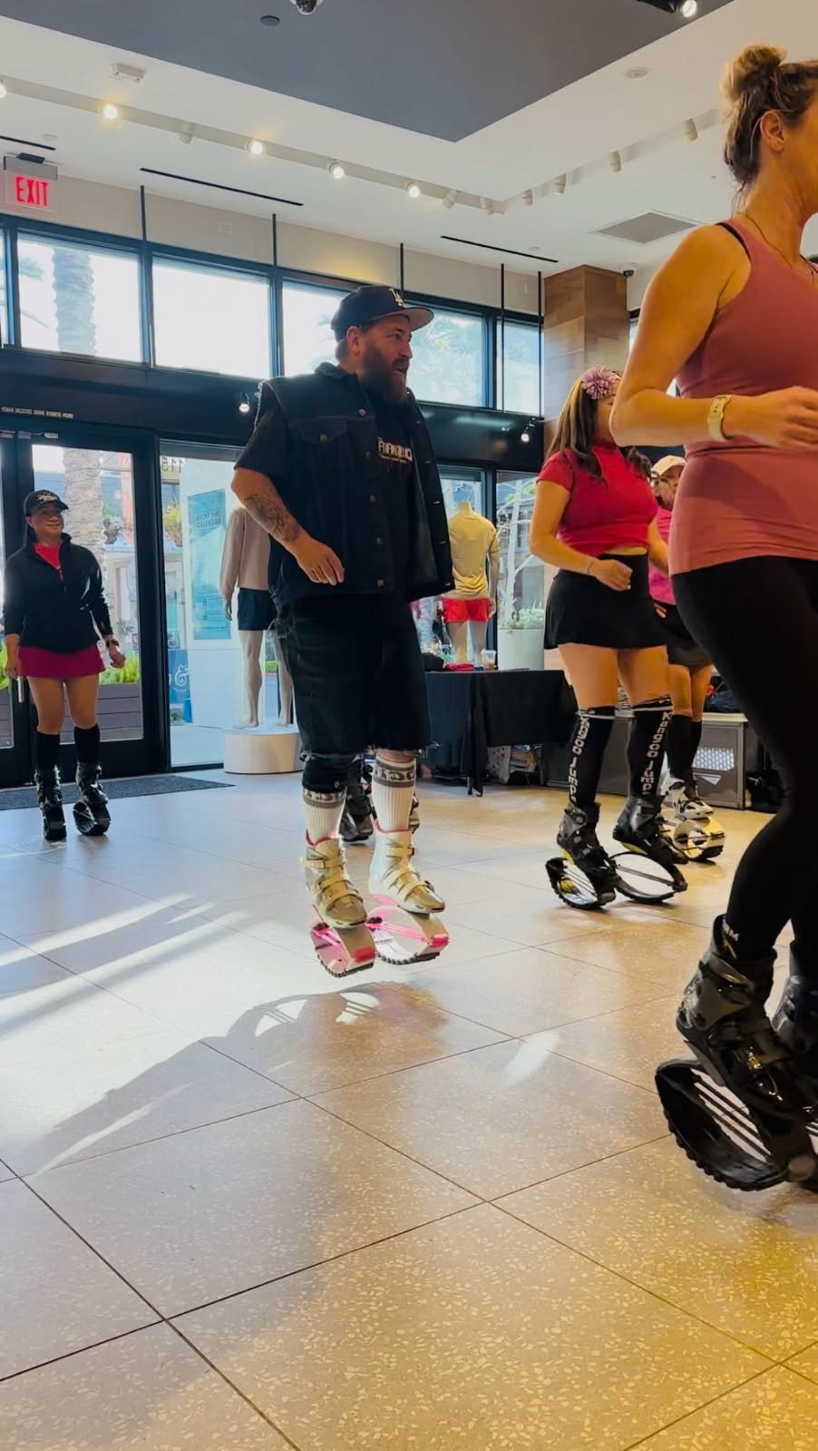 Group of people in a fitness studio wearing kangaroo jump boots, engaging in an exercise class, large windows in the background.