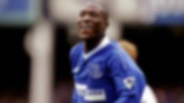 Blurred image of a soccer player wearing a blue jersey on a field.